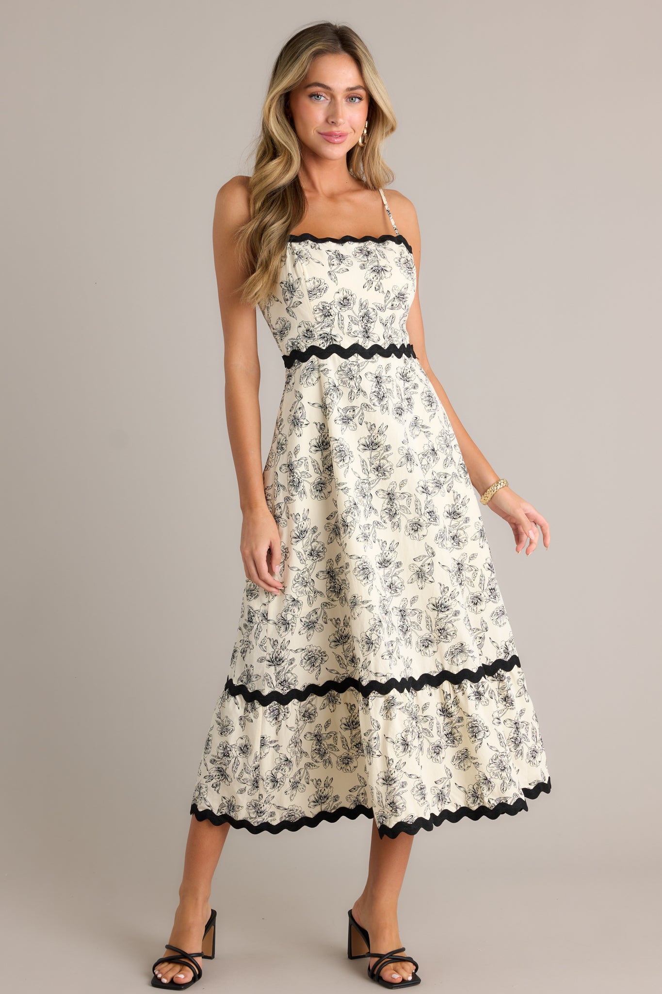 Action shot of an ivory maxi dress displaying the flow and movement of the fabric, highlighting the square neckline, black ruffle trim, tiered design, and the black floral print.