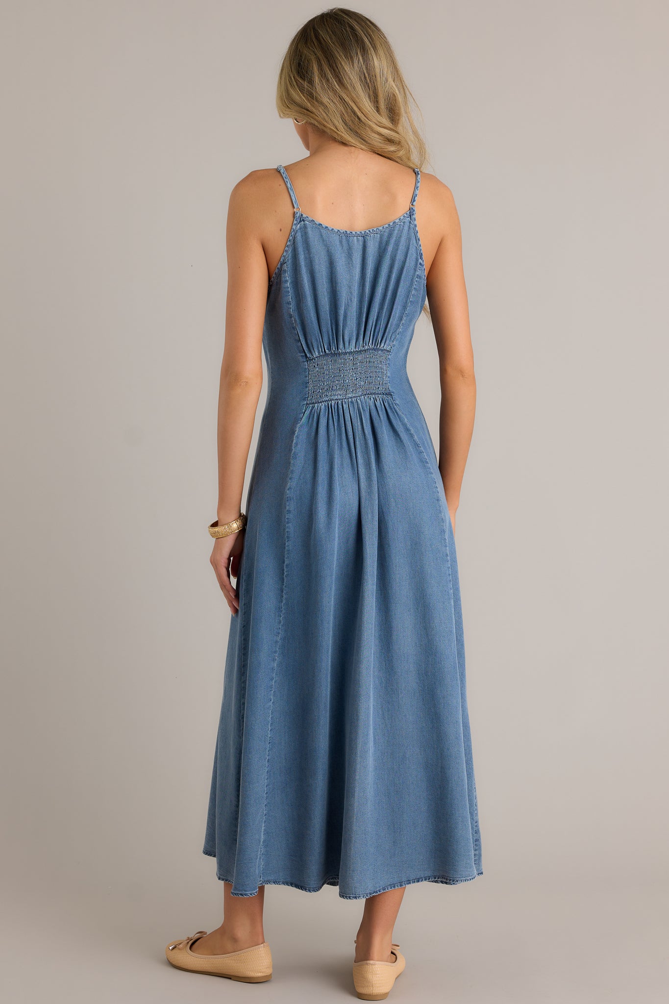 Back view of a chambray maxi dress highlighting the smocked back insert, adjustable spaghetti straps, and the overall fit.