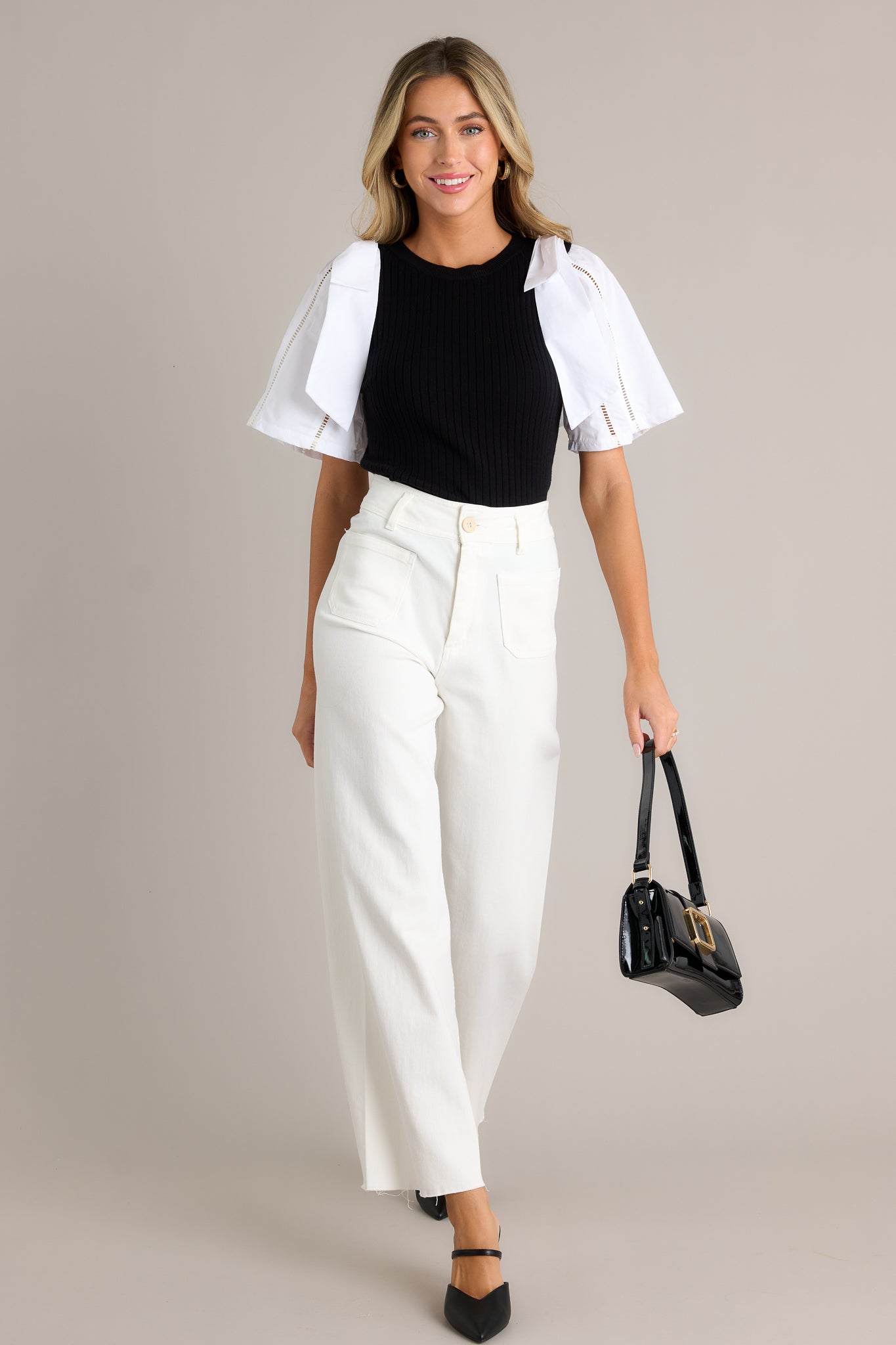 This black and white sweater top features a round neckline, a ribbed sweater bodice, color blocked cotton sleeves, bowties on each shoulder and delicate cut-out detailing on the sleeves.