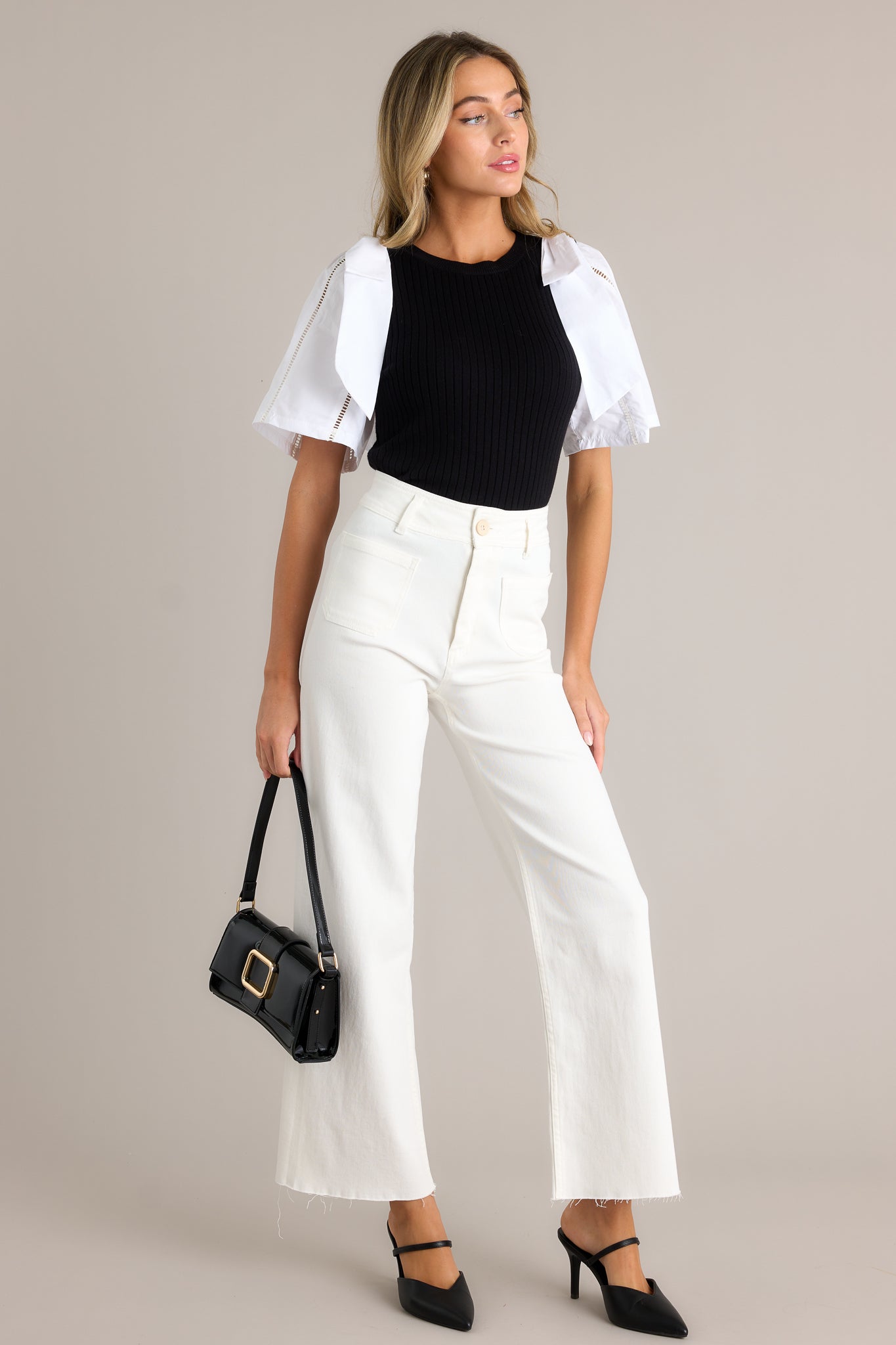 Full length view of a black and white sweater top with a round neckline, a ribbed sweater bodice, color blocked cotton sleeves, bowties on each shoulder, and delicate cut-out detailing on the sleeves