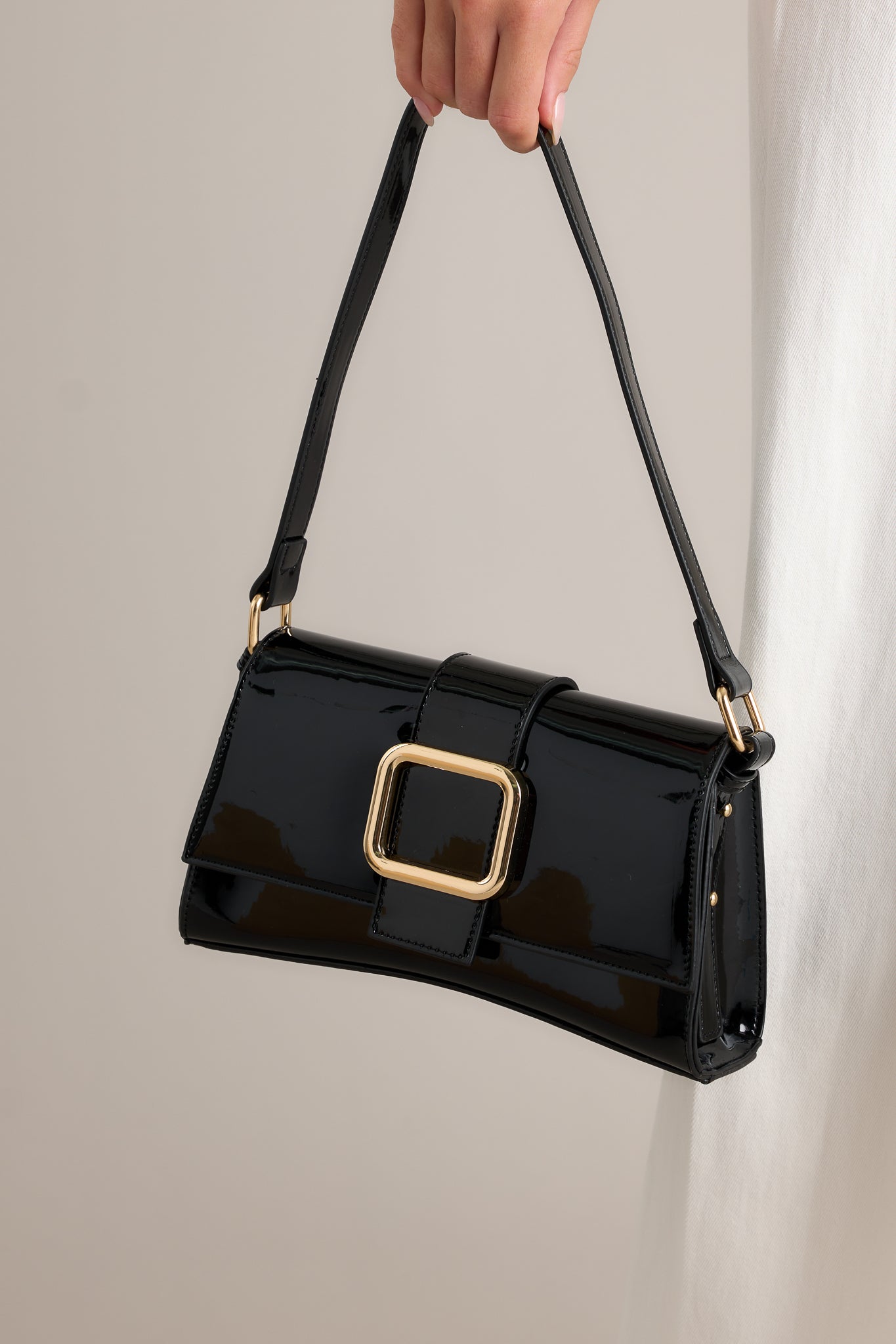 This handbag features a gold rectangular buckle, two snap clasps, interchangeable straps and a glossy chic design.