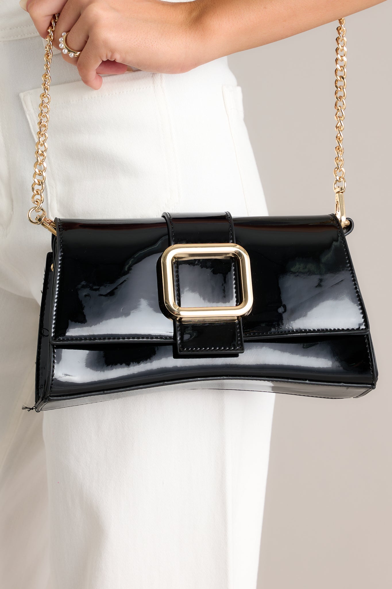 Close-up of this black handbag that features a gold rectangular buckle, two snap clasps, interchangeable straps and a glossy chic design.