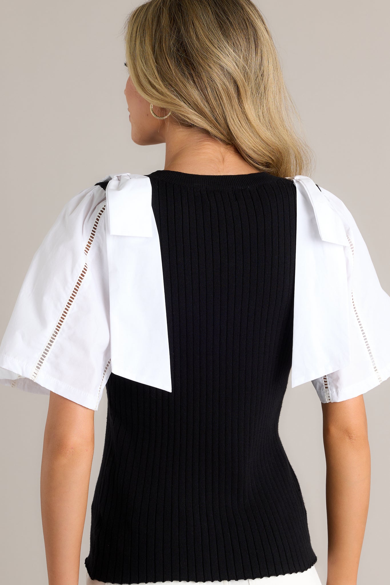 Back view of a black and white sweater top highlighting the overall fit, color blocked cotton sleeves, and the bowtie details on the shoulders.