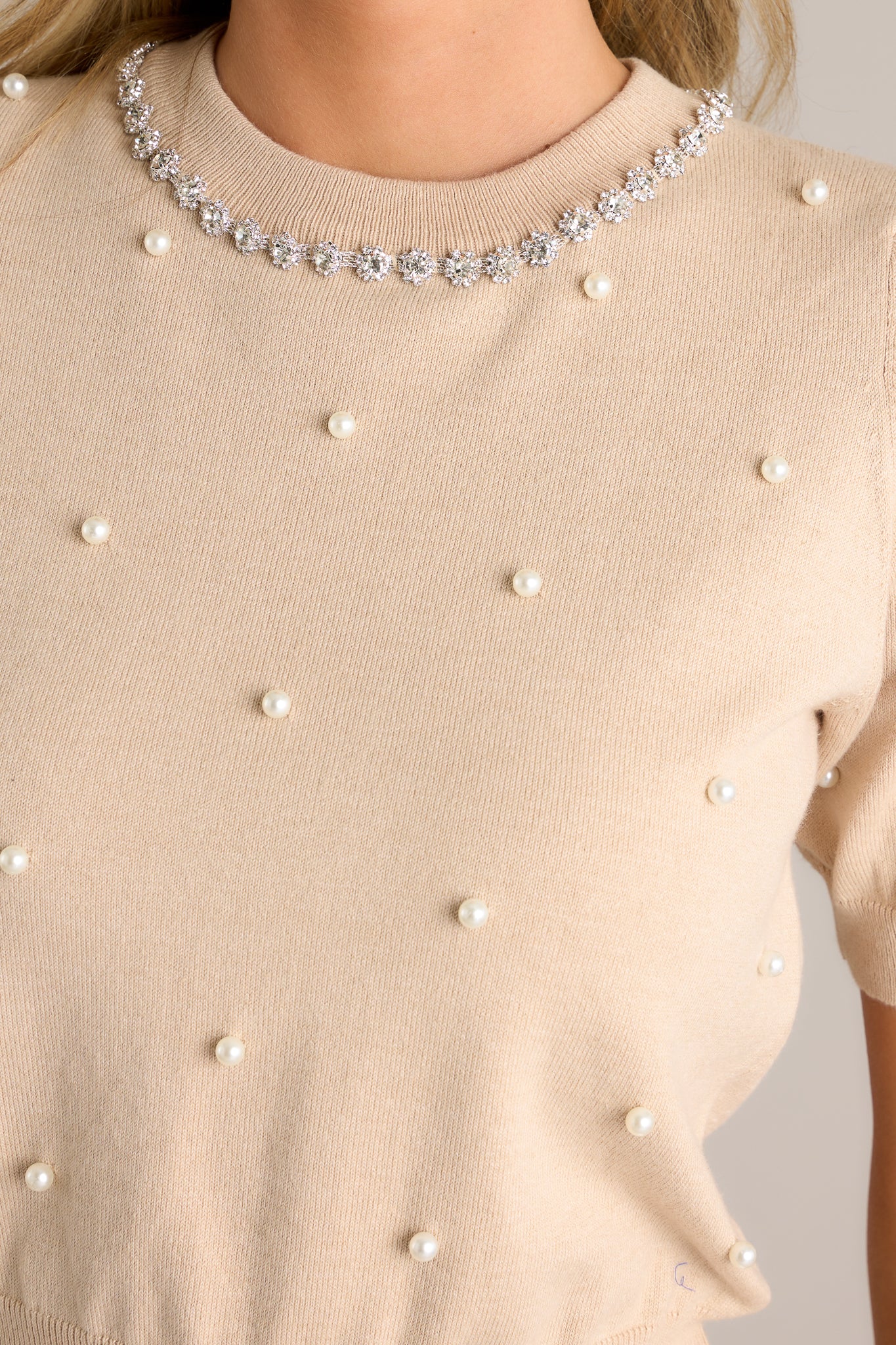 Detailed view the pearl detailing and the rhinestone collar detail on this beige short sleeve sweater top.