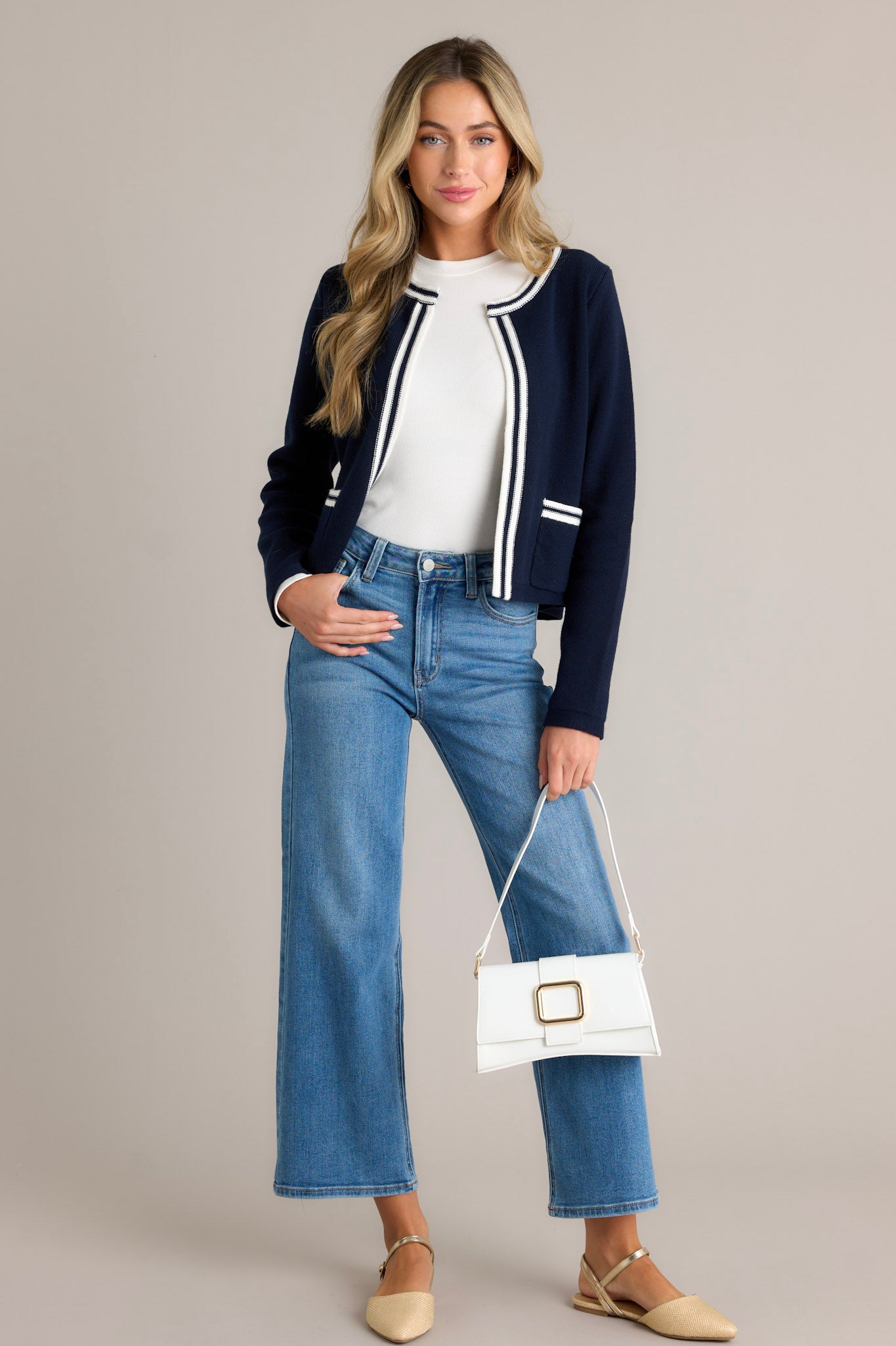 Full length view of a navy knit cardigan with an open knit design, striped detailing, two functional front pockets, and long cuffed sleeves