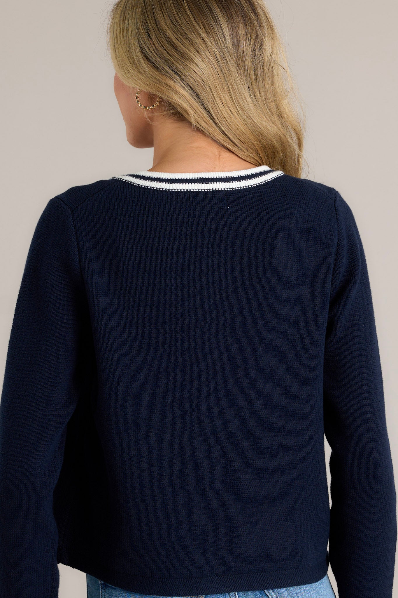 Back view of a navy knit cardigan highlighting the open knit pattern, striped detailing, and the overall structure of the long cuffed sleeves.