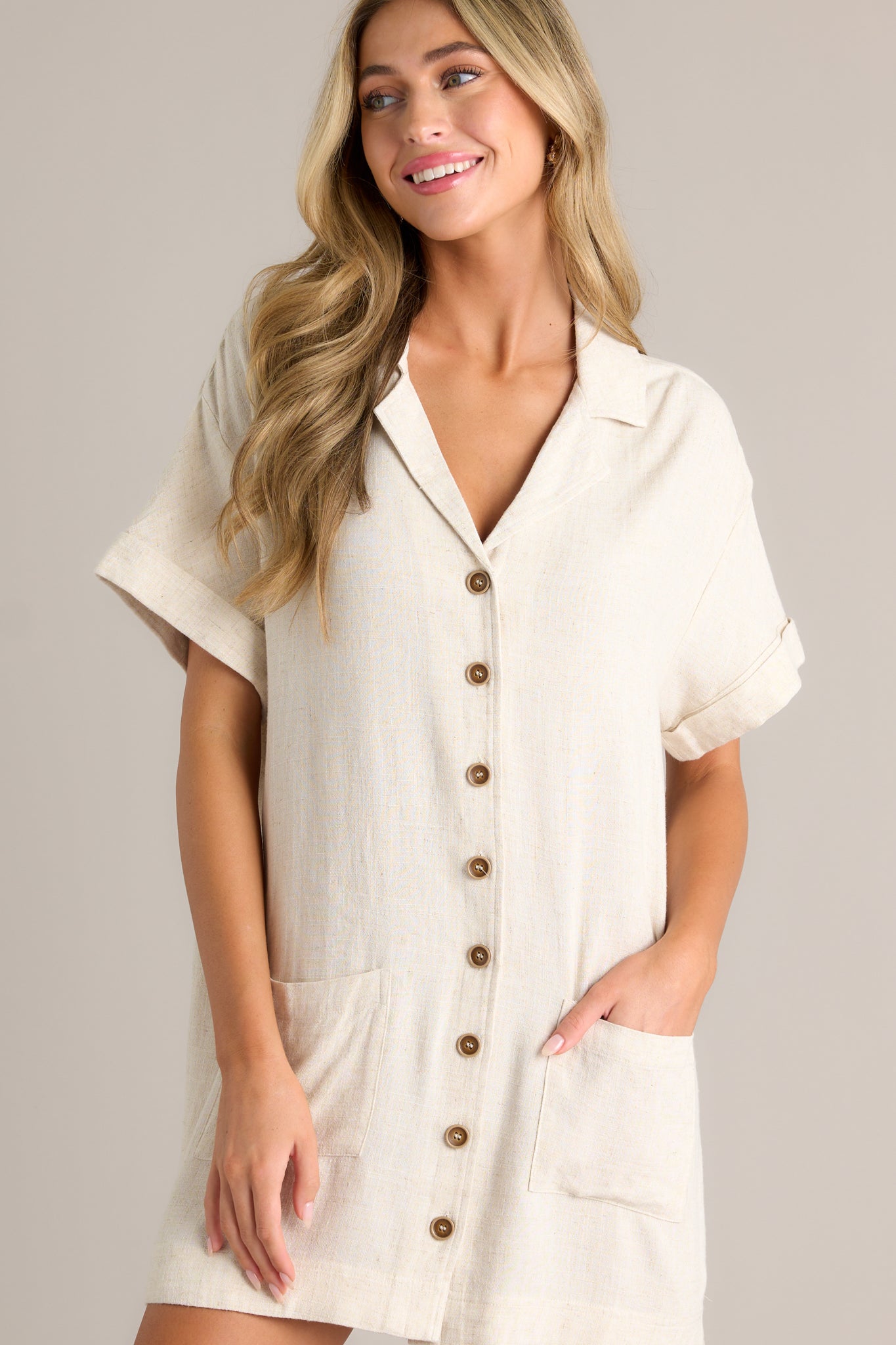 Action shot of a beige dress displaying the fit and movement, highlighting the collared v-neckline, functional button front, hip pockets, short cuffed sleeves, and relaxed fit.