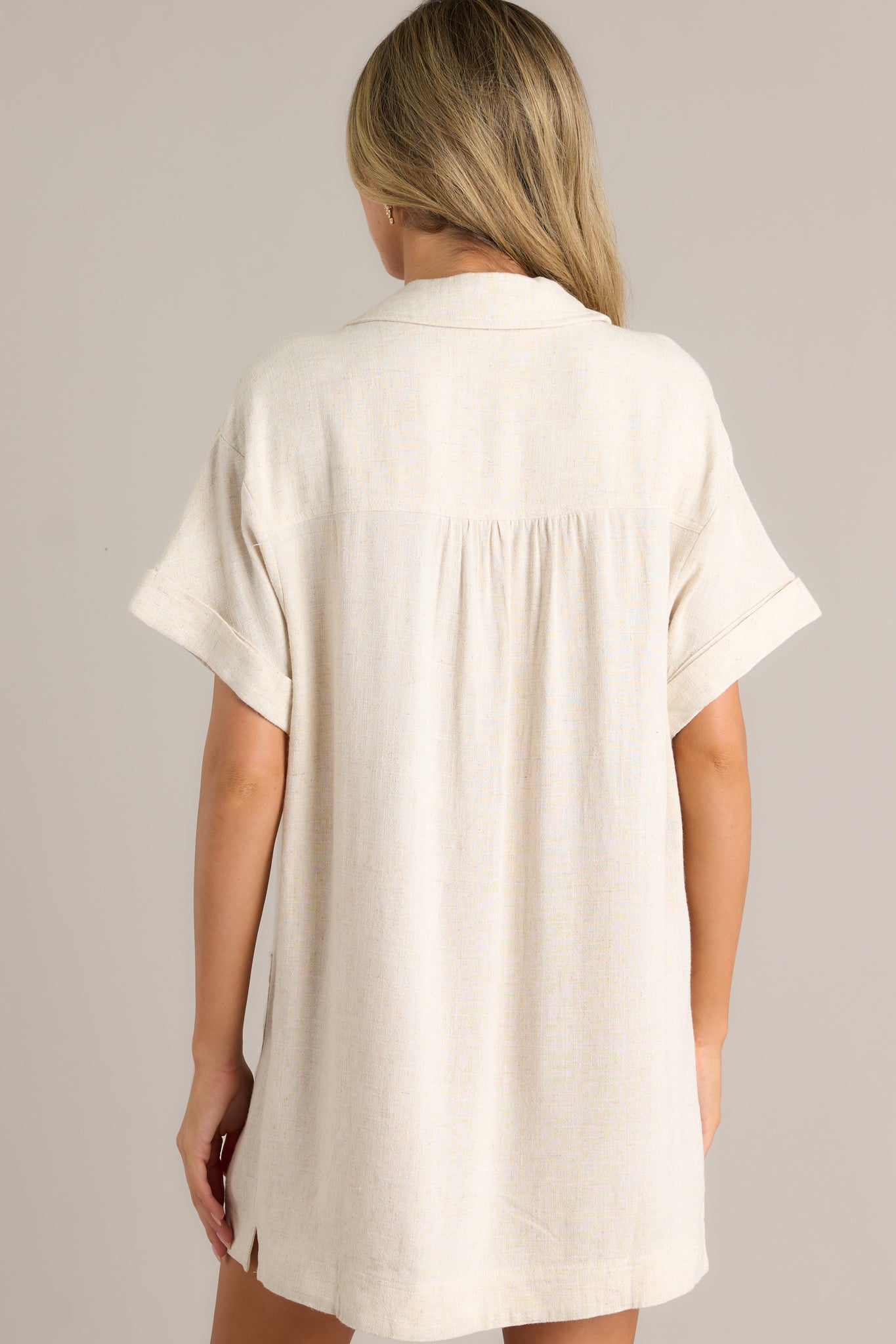 Back view of a beige dress highlighting the overall fit, collared neckline, and short cuffed sleeves.