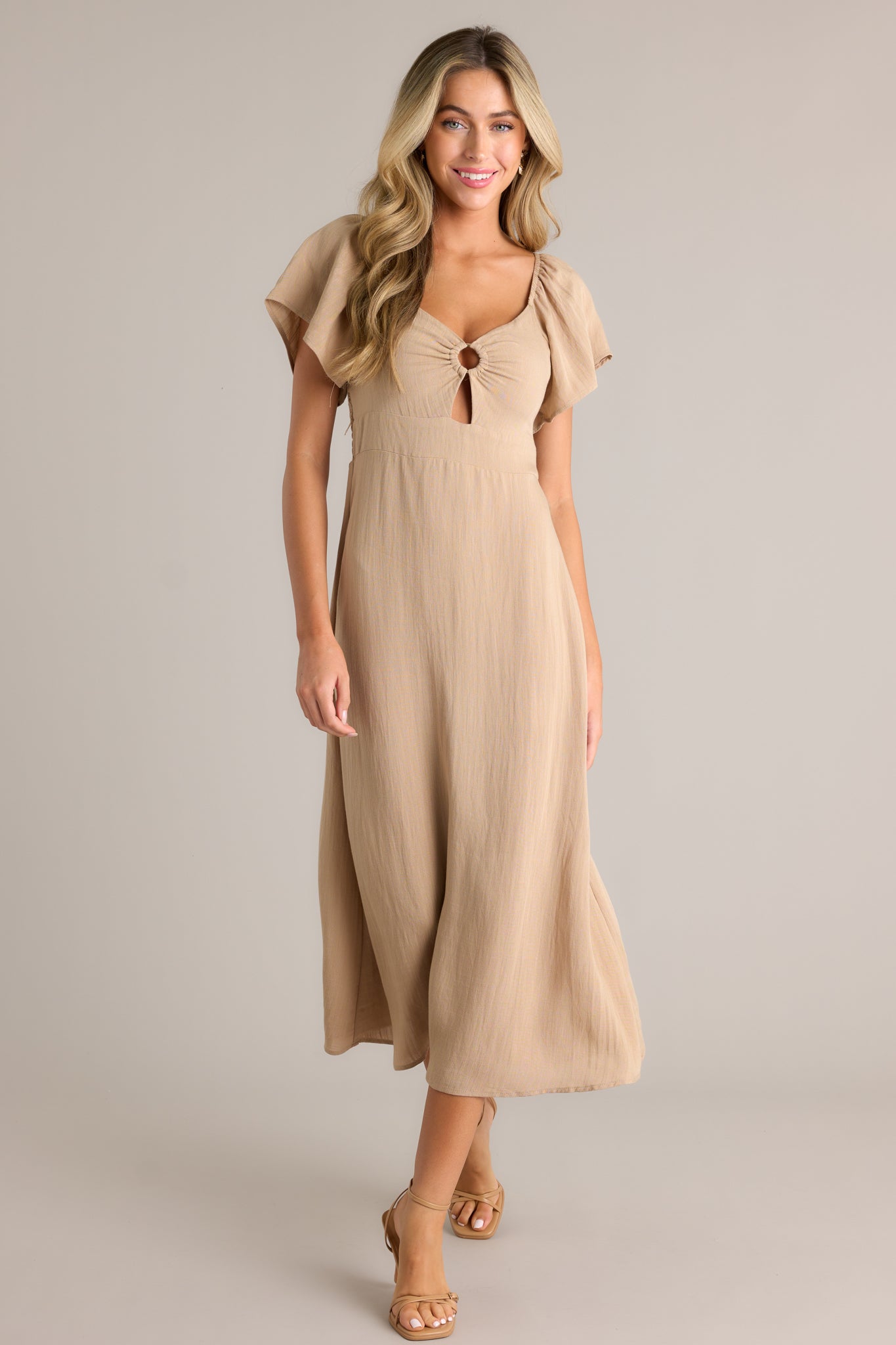 This midi dress features a cut-out design in the chest, a smocked back, elastic cuffed puff sleeves, an accent gold ring in the bust, and a flowing silhouette.