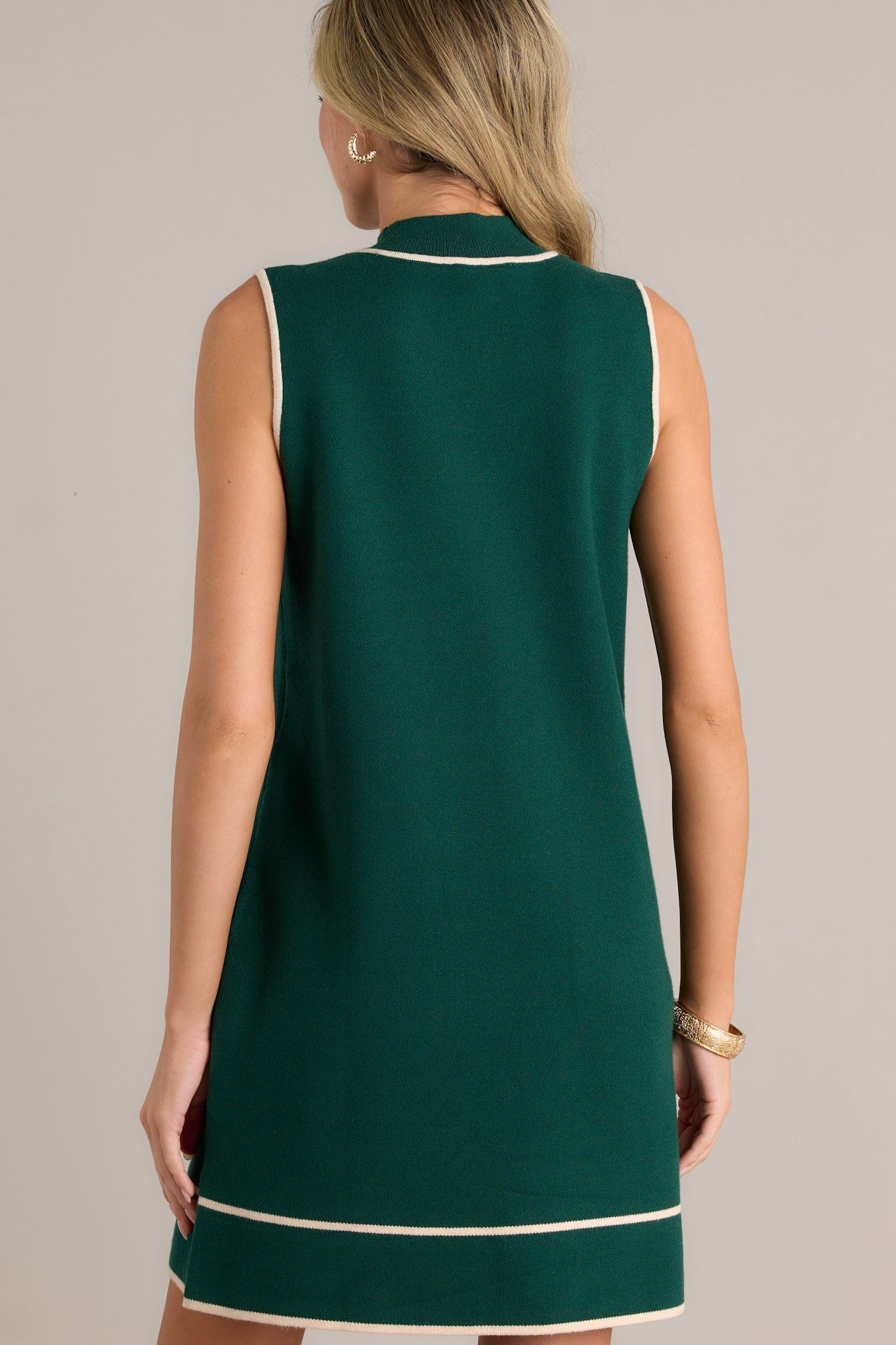 Back view of a green dress highlighting the sleeveless design, beige trim, and ribbed high neckline.