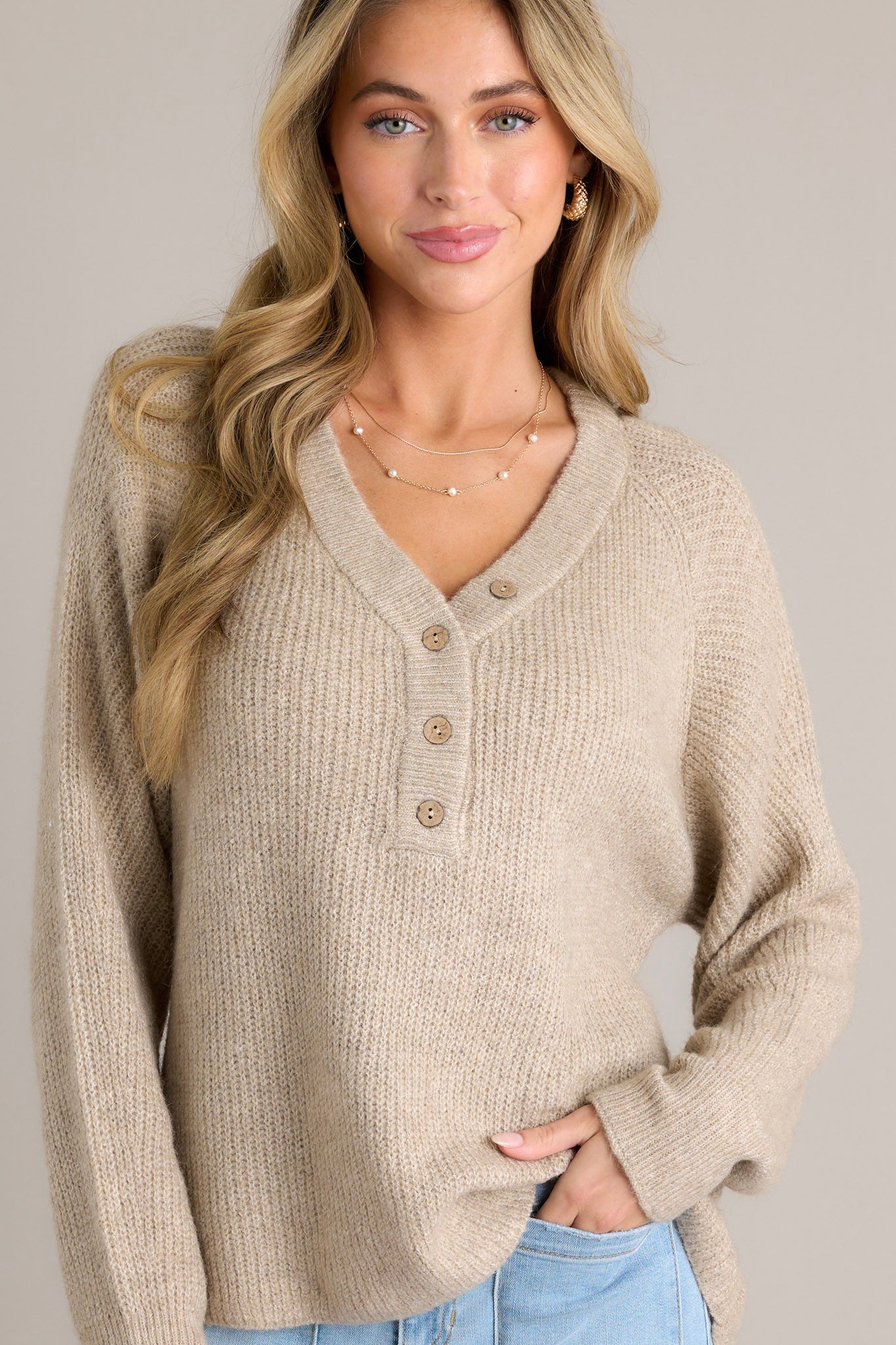 Front view of a sweater featuring a v-neckline, functional buttons down the front, ribbed detailing throughout, and ribbed ruffled long sleeves.