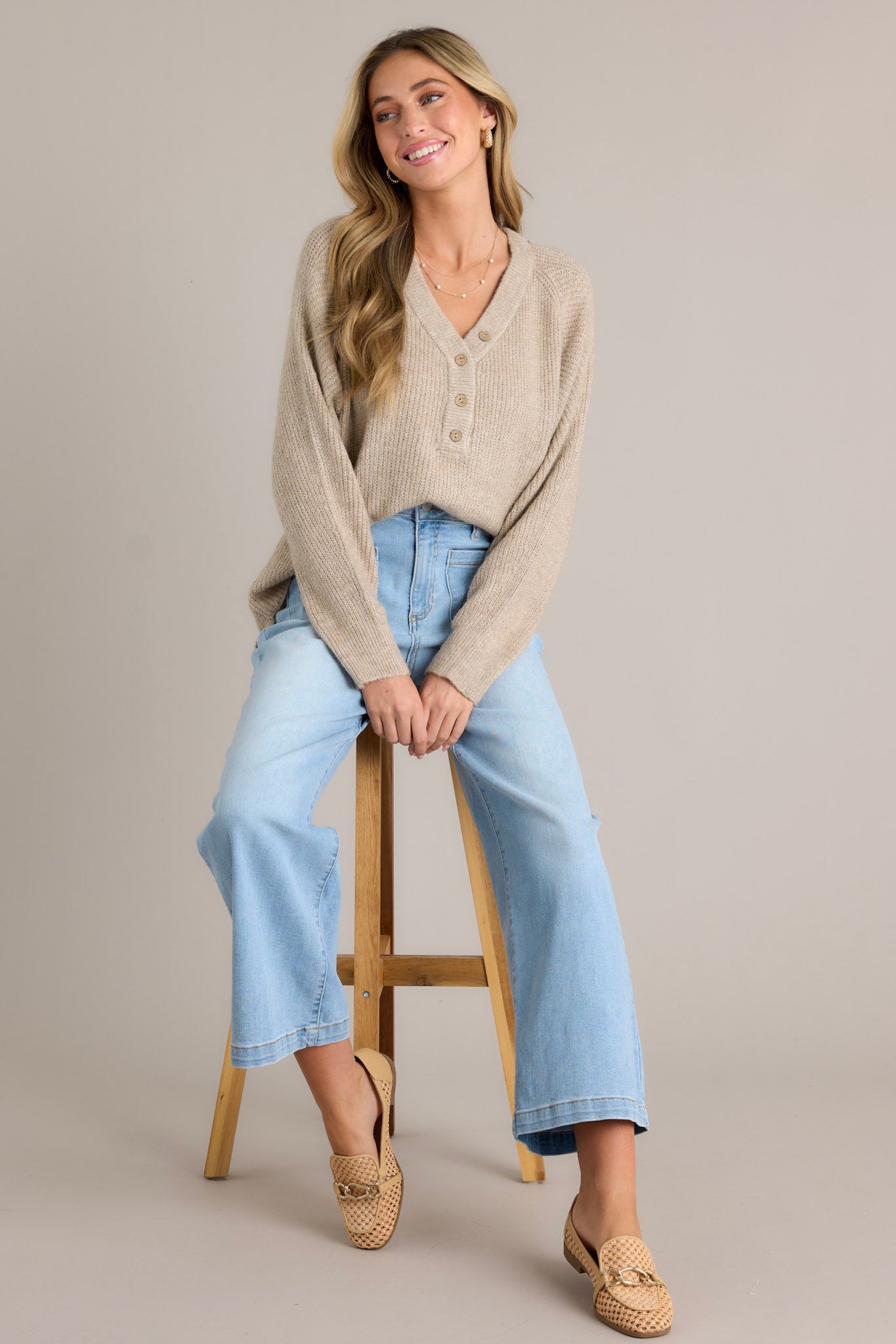 Seated Full length view of a sweater featuring a v-neckline, functional buttons, ribbed detailing throughout, and ribbed ruffled long sleeves