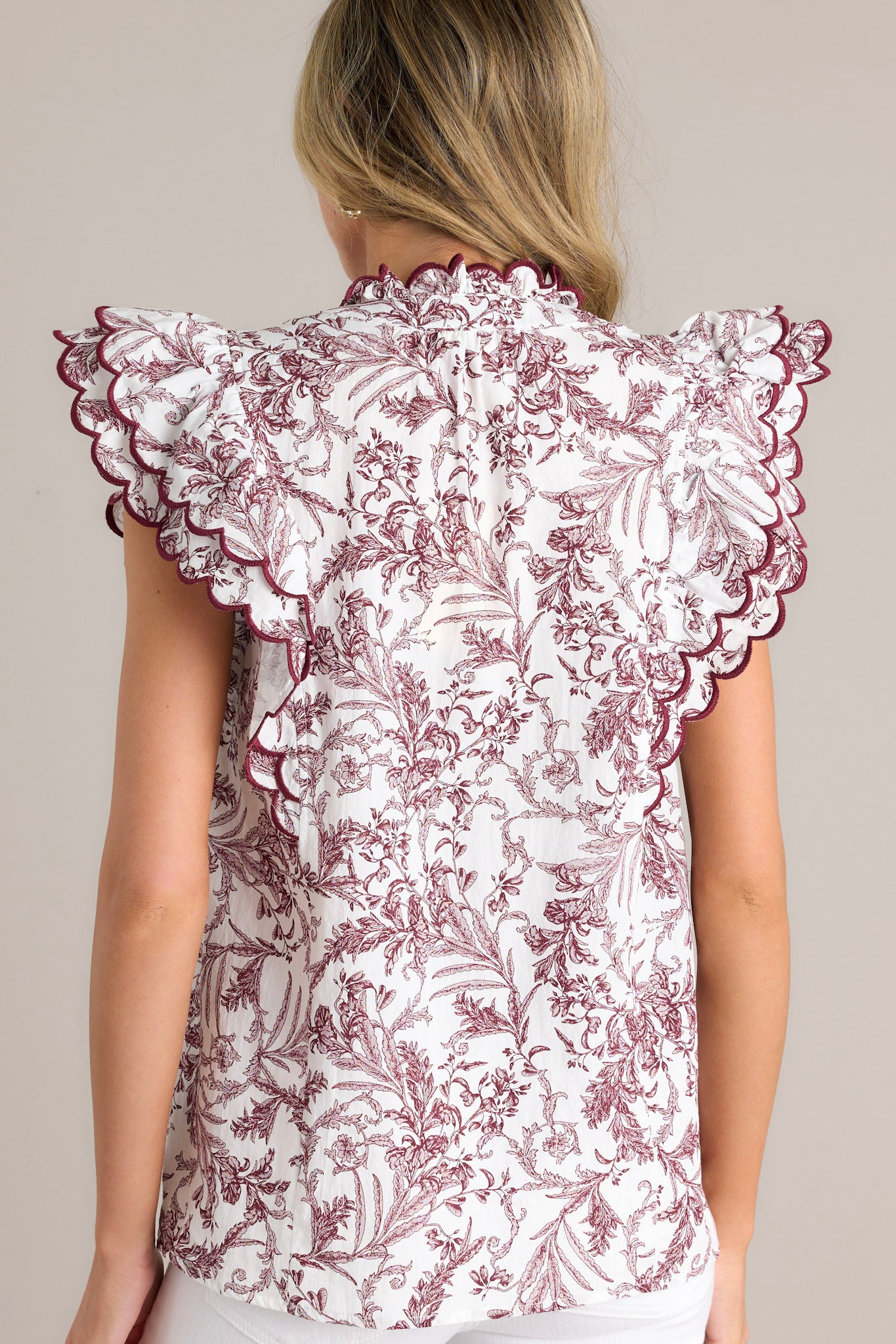 Back view of this burgundy top featuring a ruffled collar, a v-neckline, a burgundy toile print and tiered short ruffle sleeves.