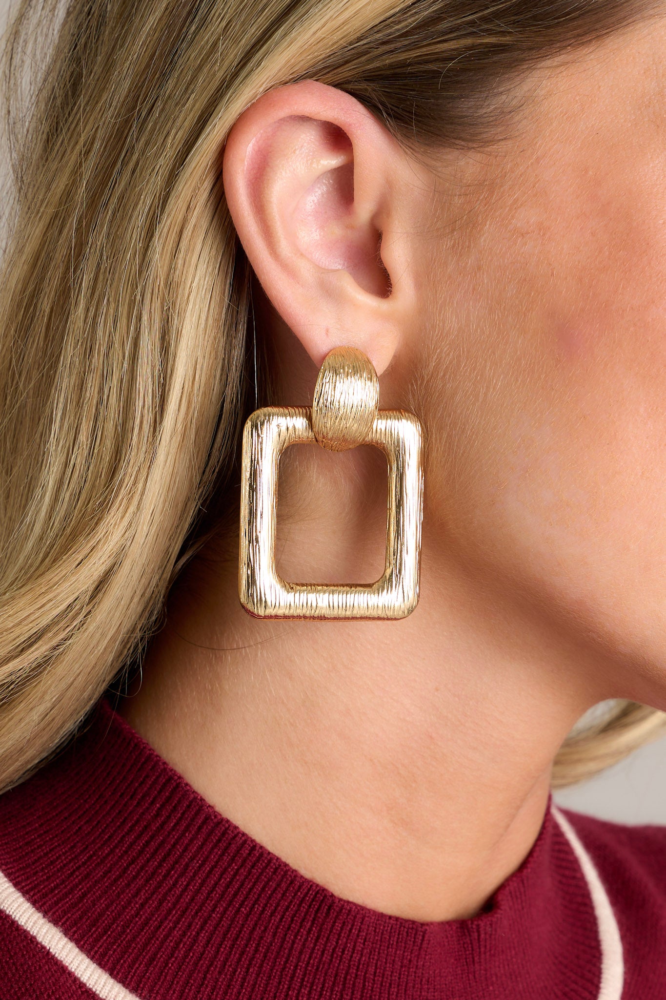 These gold earrings feature textured gold hardware, a textured stud with a connected textured square hoop, and secure post backings.