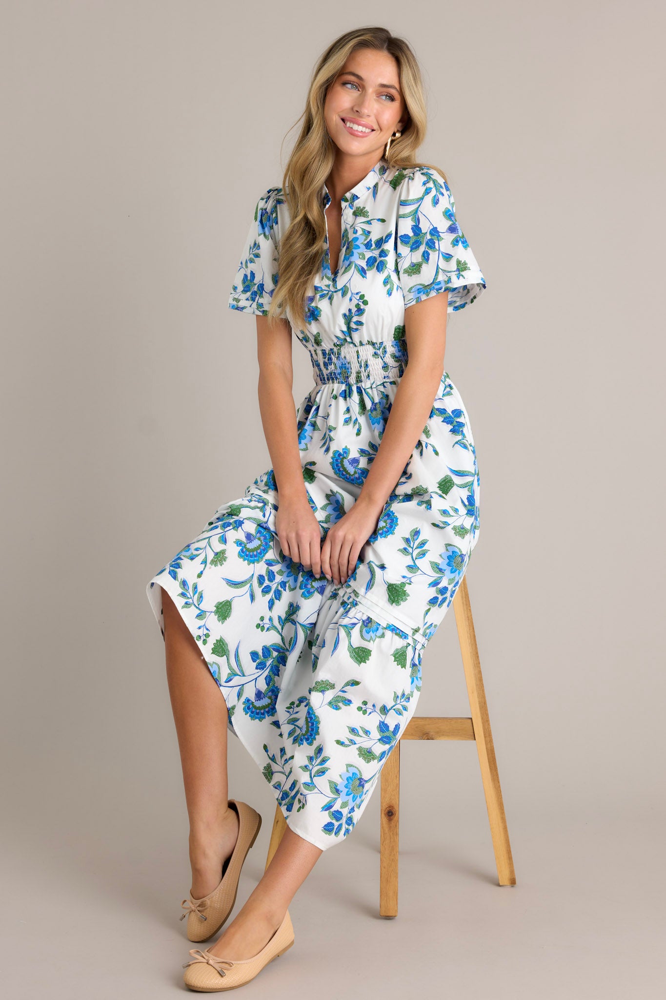 Seated Full length view of a blue floral dress featuring a stretchy waistband, a small V-neck, and blue appliqué florals