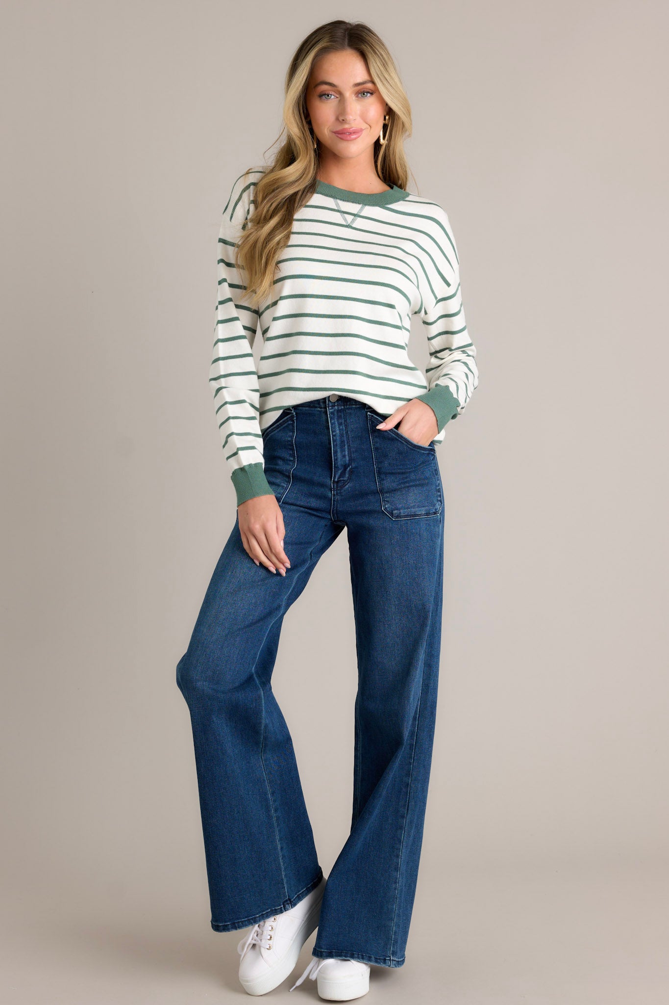 Full length view of a striped long sleeve top with a rounded neckline, green horizontal stripe design, green trim, long cuffed sleeves, and a thick hem with side slits