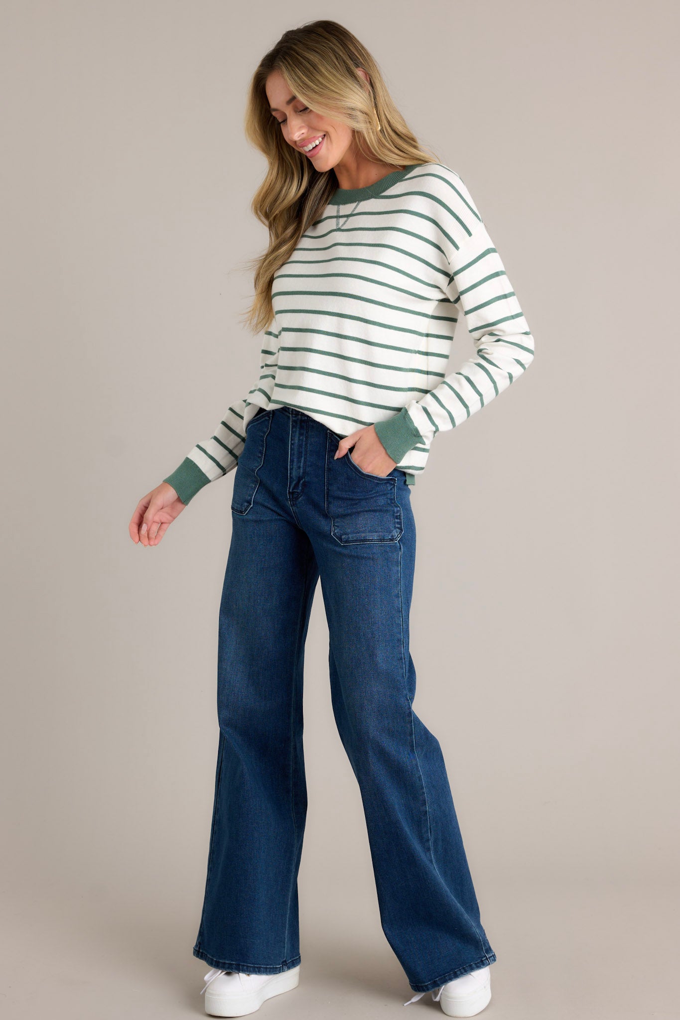 Side view of a striped long sleeve top showcasing the rounded neckline, green horizontal stripe design, green trim, long cuffed sleeves, and thick hem with side slits.