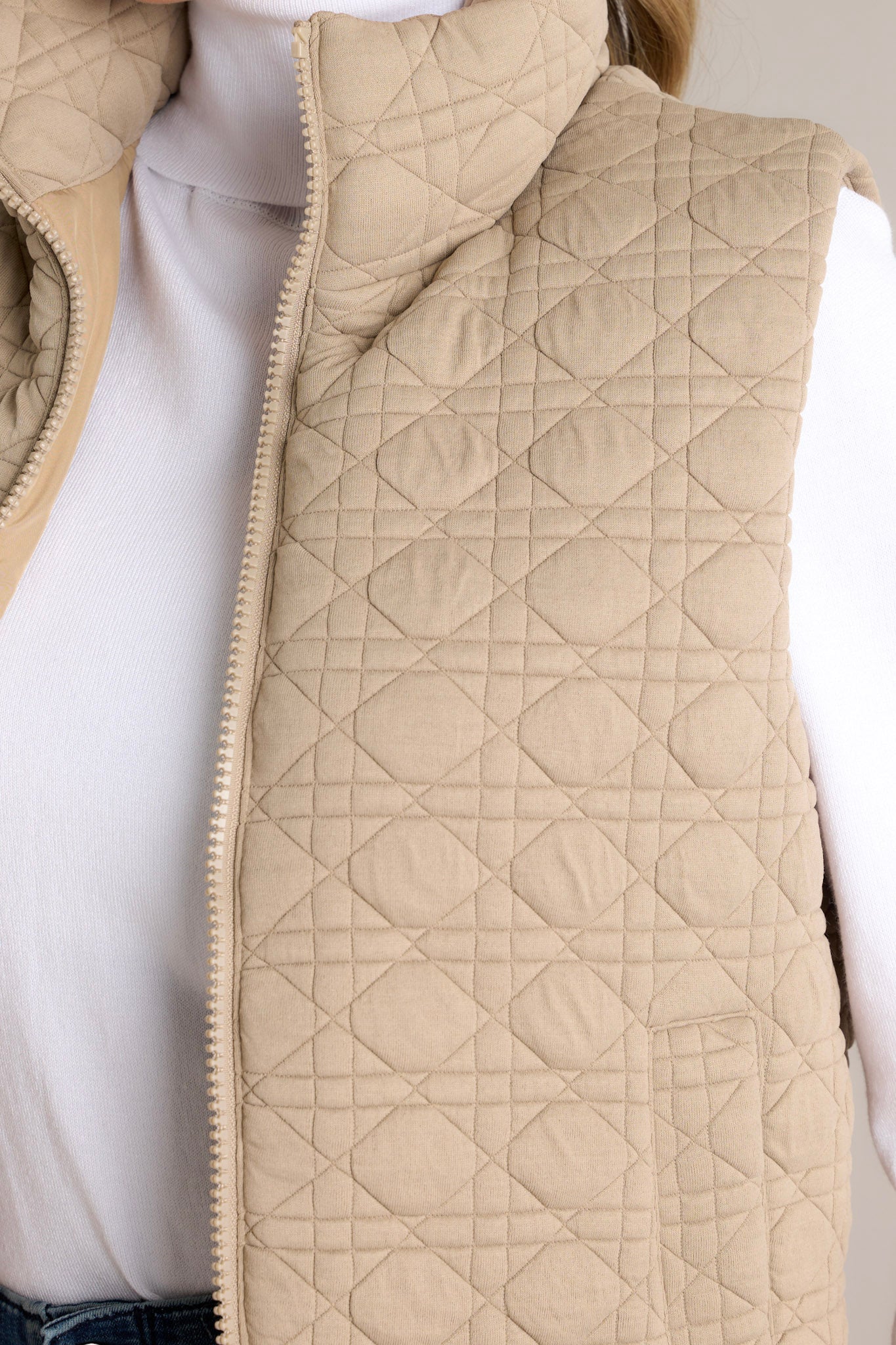 Close-up of the tan vest's quilted pattern, zip closure, and functional pocket.