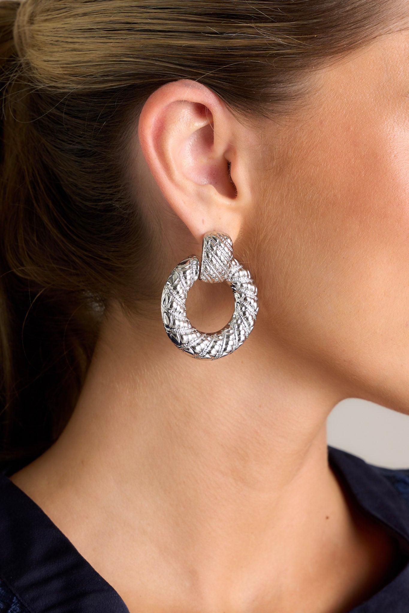 These silver earrings feature&nbsp;a ridged stud with a connected ridged hoop with the ridges increasing in size.