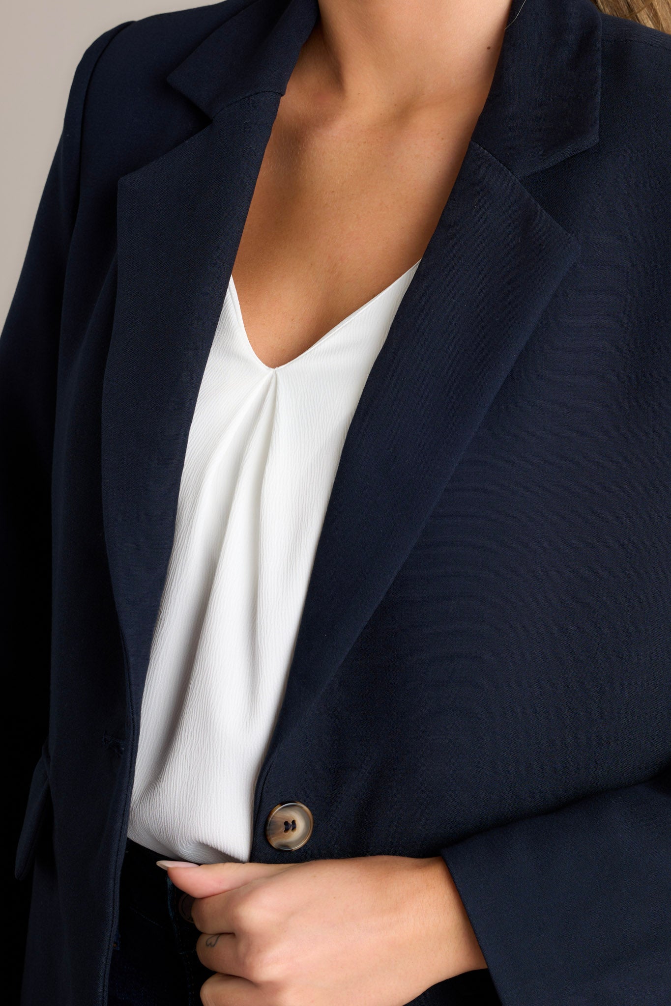 Close-up of a navy blazer showing the collared neckline, middle button closure, floral lining, and padded shoulders.