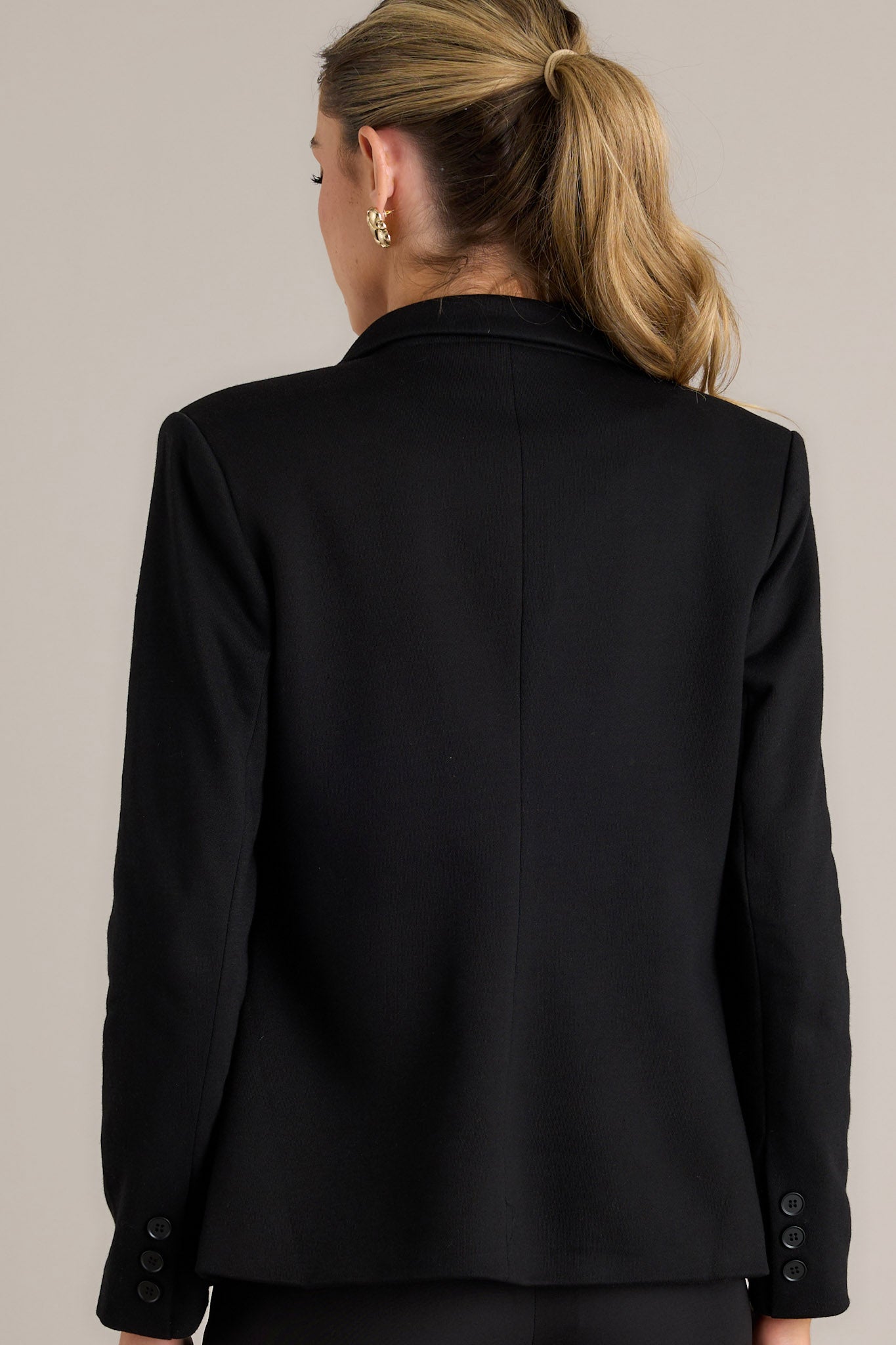 Rear view of the black blazer showing the clean lines, padded shoulders, and the back seam detailing.