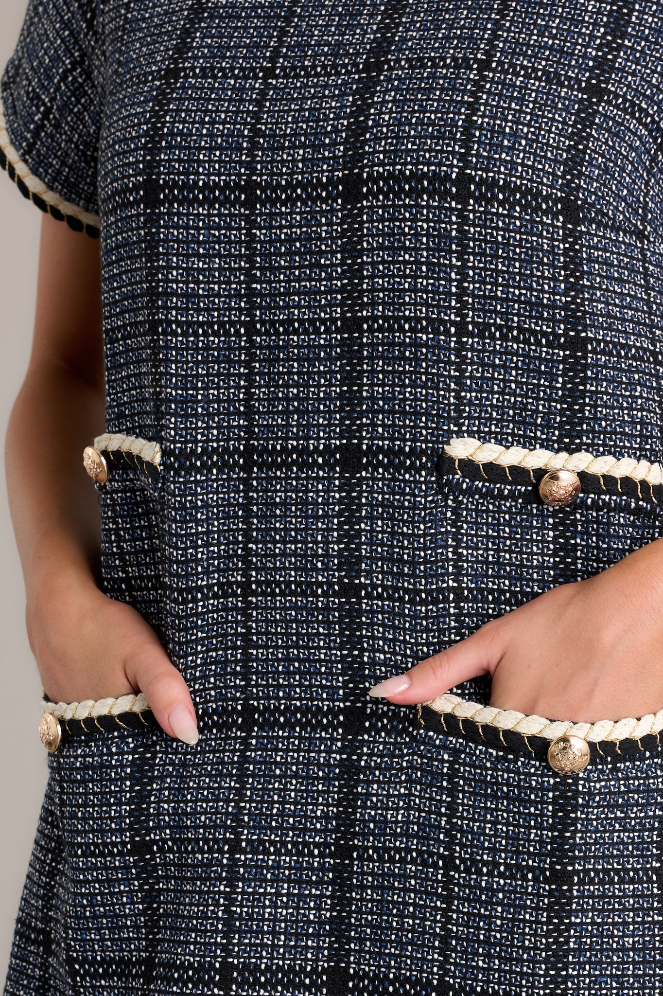 Close-up of the tweed dress showing the rounded neckline, ivory trim, gold accent buttons on the functional hip pockets, and the tweed fabric texture.