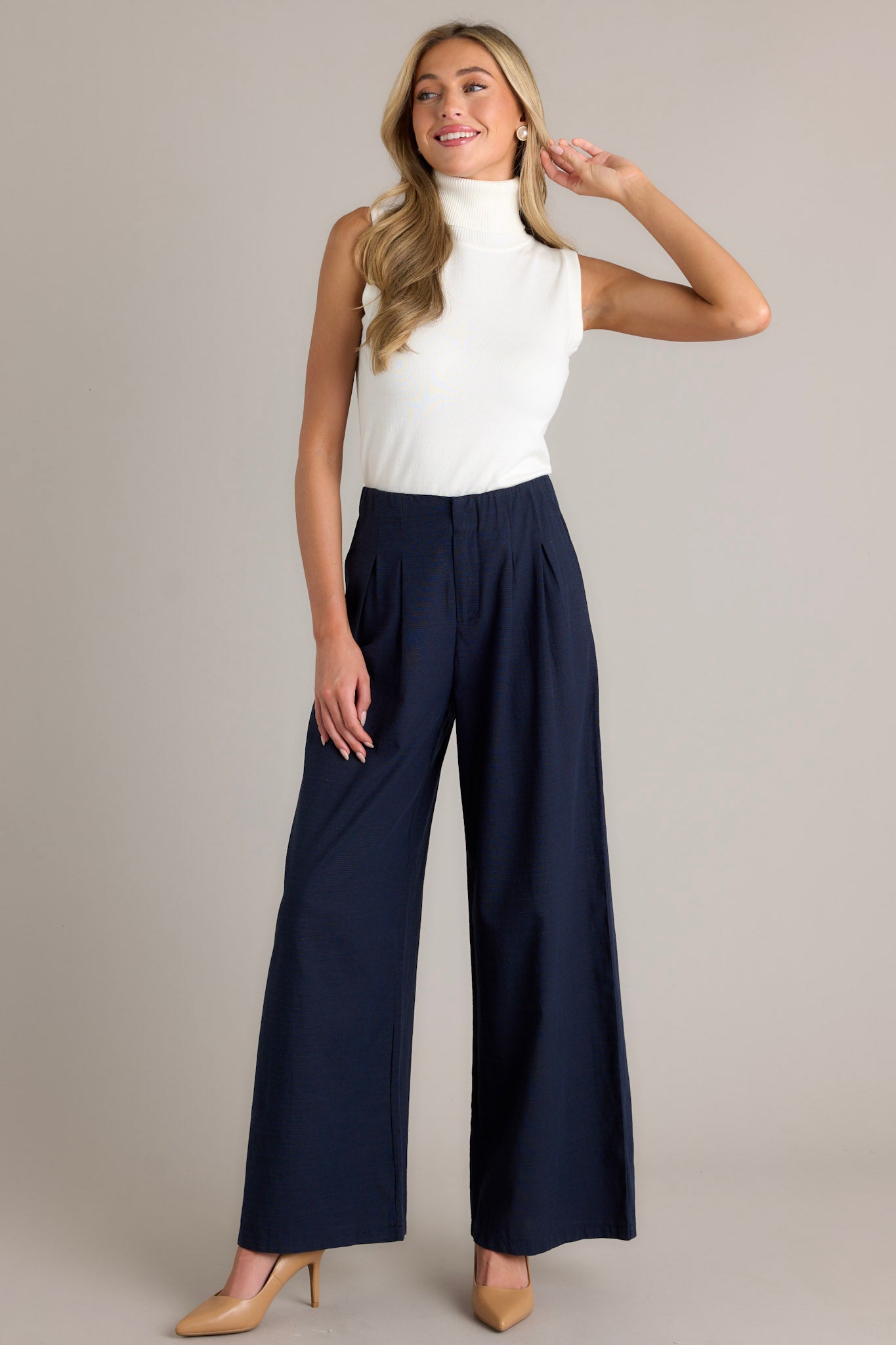 Action shot of navy straight leg pants displaying the fit and movement, highlighting the high waisted design, button zipper closure, slight pleats, and functional hip pockets.