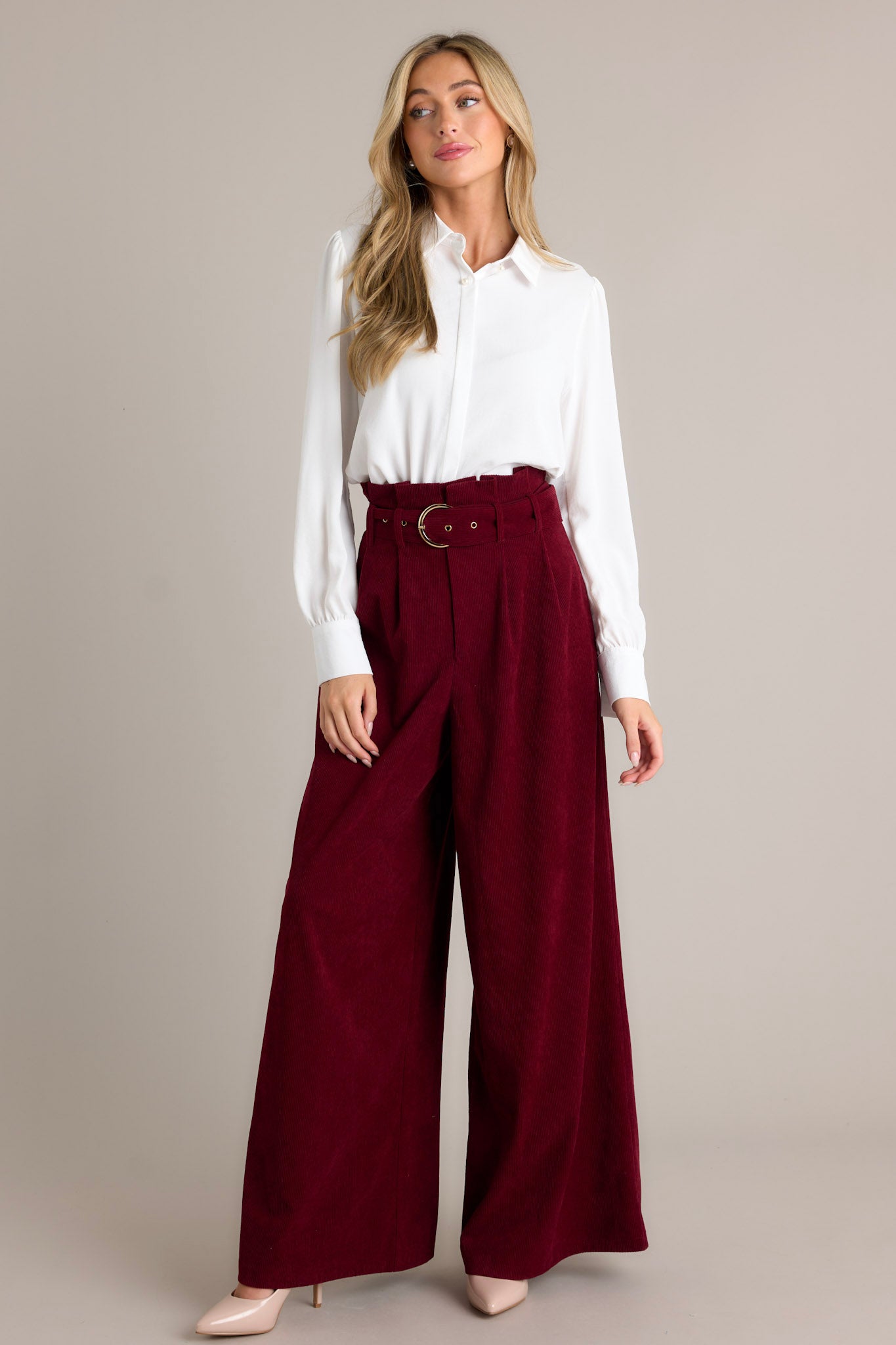 Front angled view of burgundy pants featuring a paper bag style waistline, an adjustable belt, a zipper closure, and very flowy legs