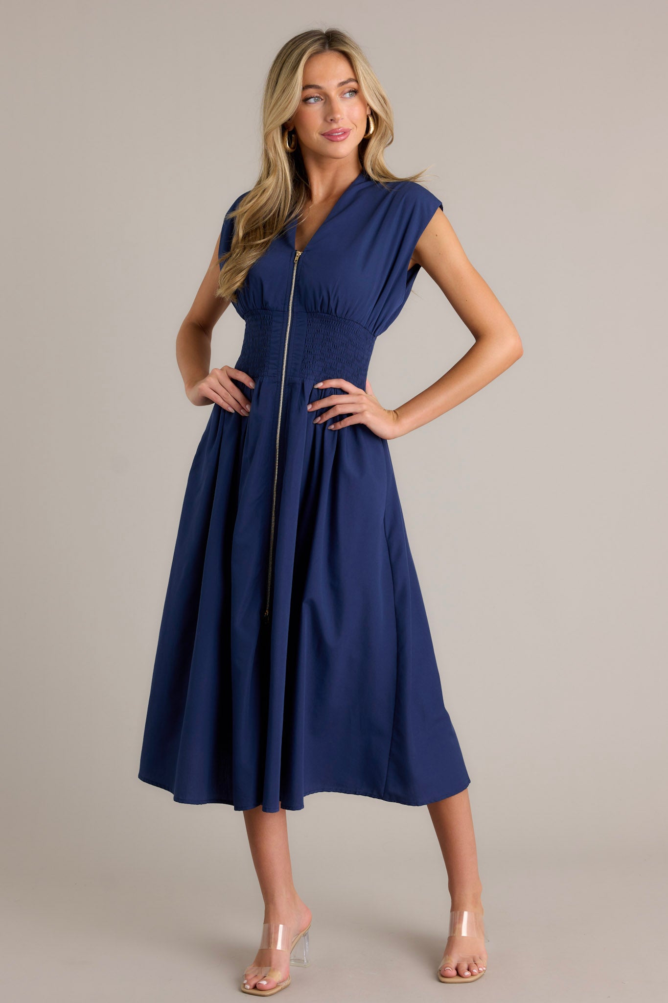 Front view of a navy blue dress featuring a V-neckline, cap sleeves, a zippered front, and a cinched waist with shirred detailing, highlighting its stylish and elegant design.