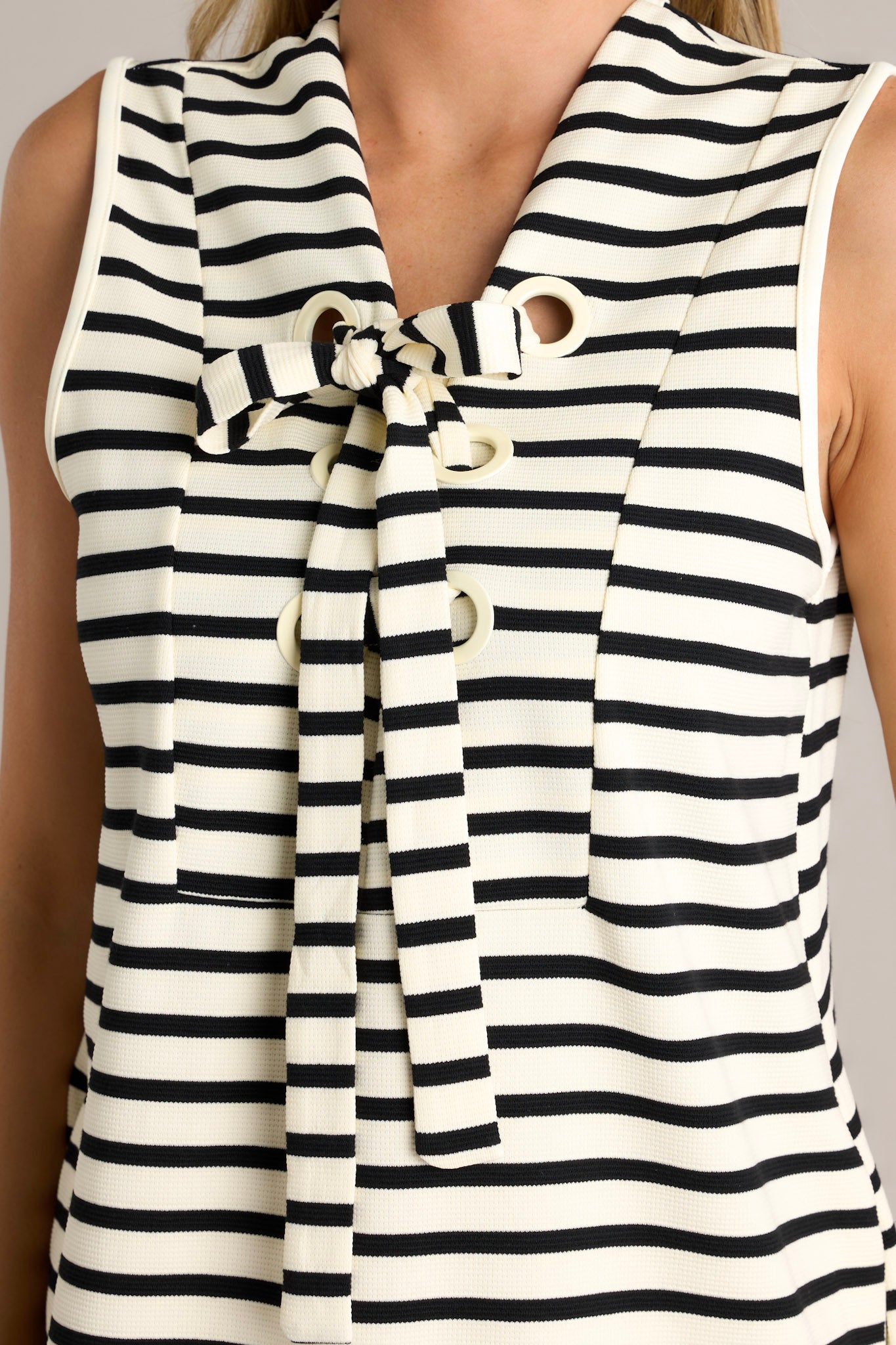 Close-up of the bow at the neckline on the sleeveless, black and ivory striped dress.