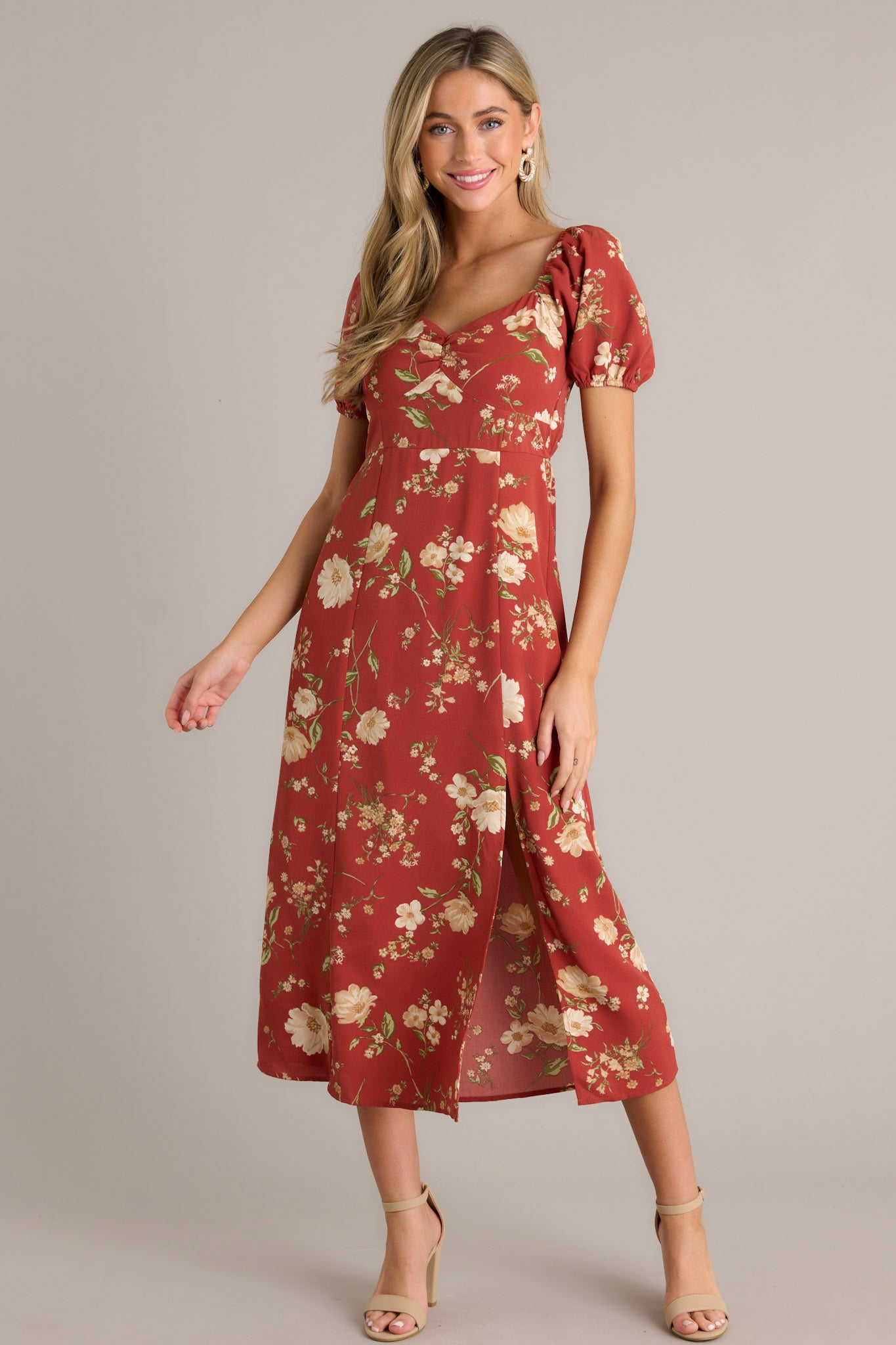 Front view of this burnt orange dress that features a square neckline with a slight v-neckline, a floral design, a smocked back insert, a slit in the left leg and short cinched puff sleeves.