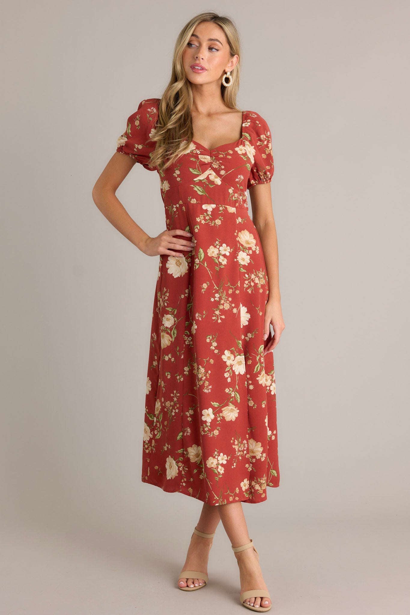 This burnt orange dress features a square neckline with a slight v-neckline, a floral design, a smocked back insert, a slit in the left leg and short cinched puff sleeves.