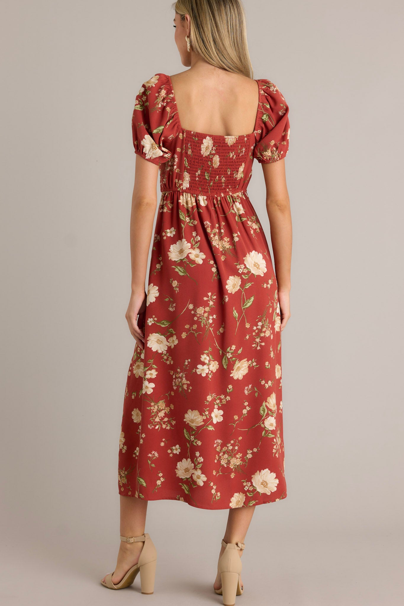 Back view of this burnt orange dress that features a square neckline with a slight v-neckline, a floral design, a smocked back insert, a slit in the left leg and short cinched puff sleeves.