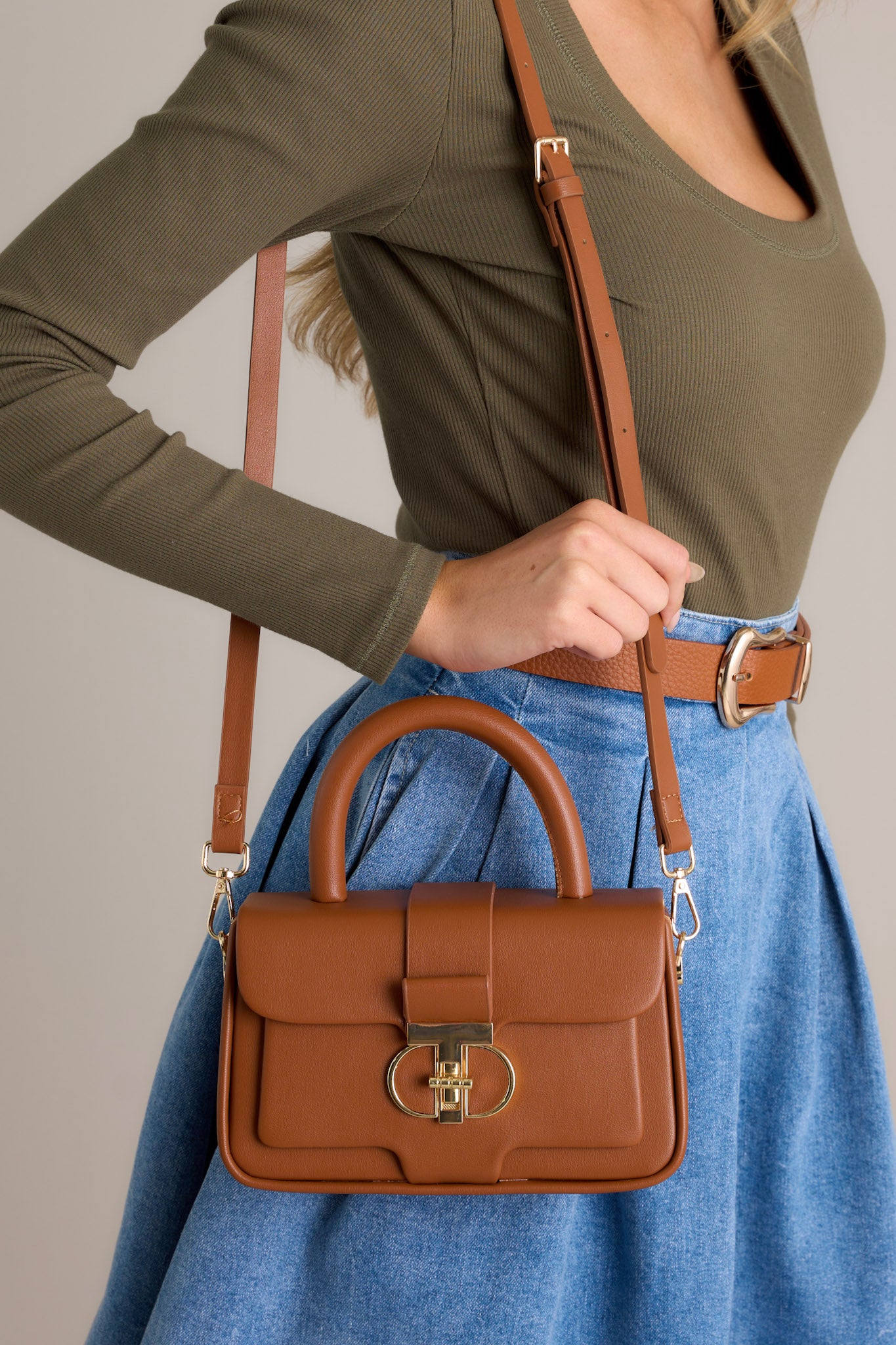 Full view of this brown handbag that features a gold accent turn closure, a built in pocket, a matching mini wallet and gold accent side loops for exchangeable straps.