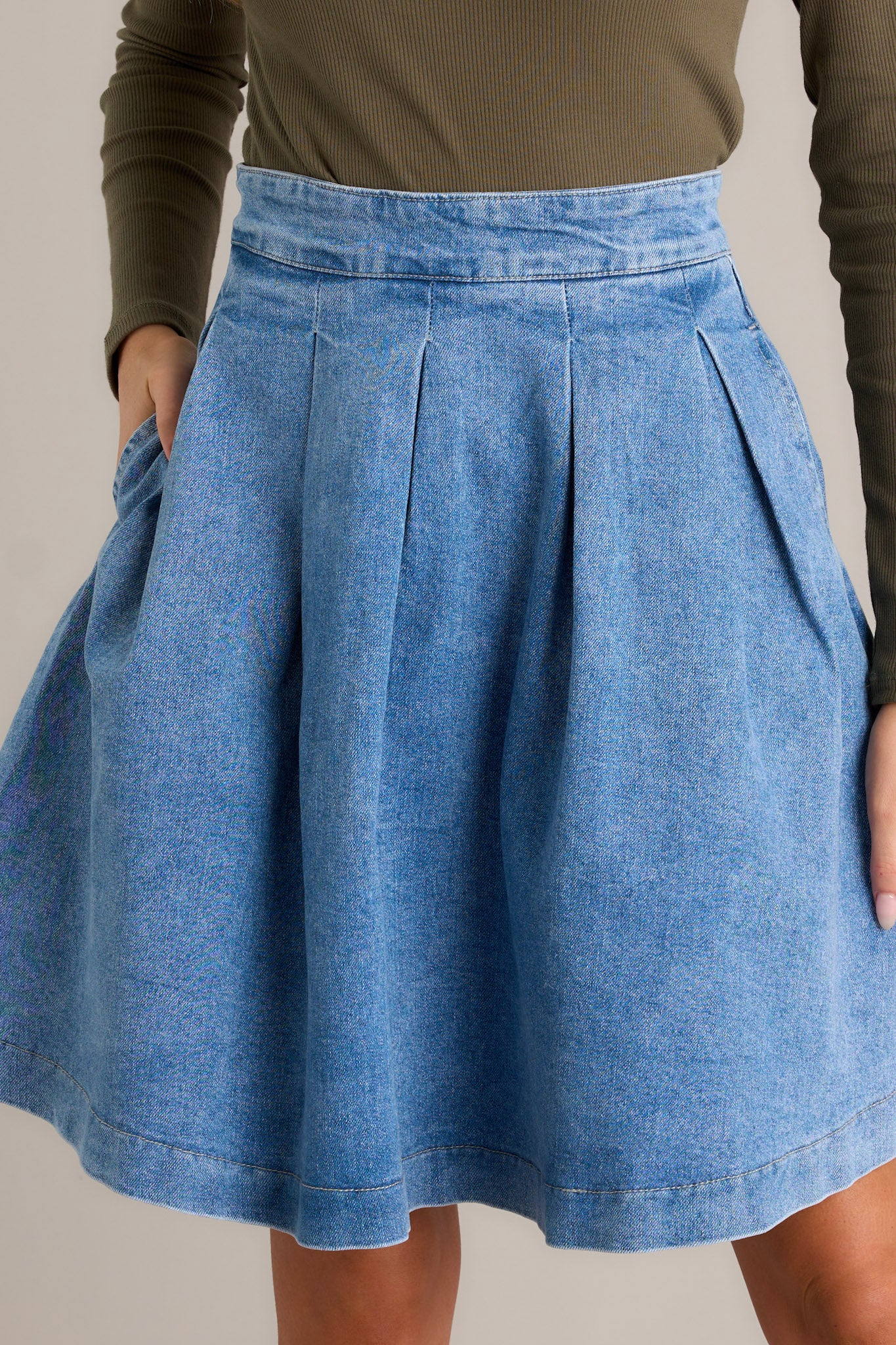 Close-up of the denim skirt showing the subtle pleats, functional hip pockets, and the back zipper closure.