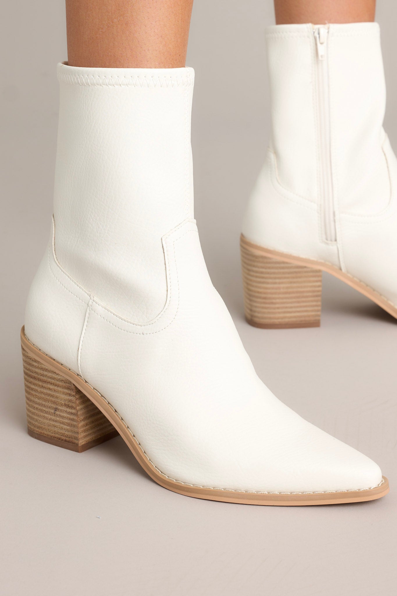 Close-up view of these white boots that feature a pointed toe, a platform heel, a discrete side zipper and a tan sole.