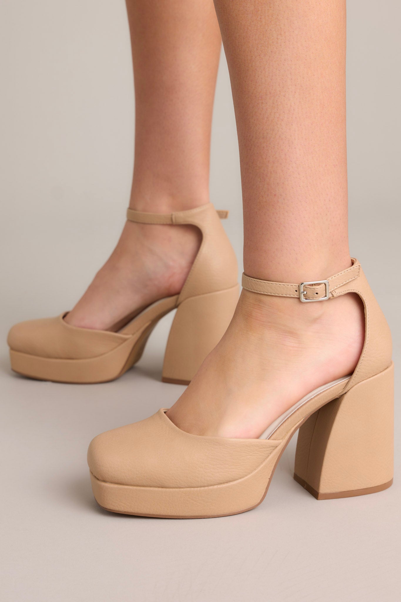 These beige heels feature an adjustable ankle strap, thick block heel, and a closed toe design.