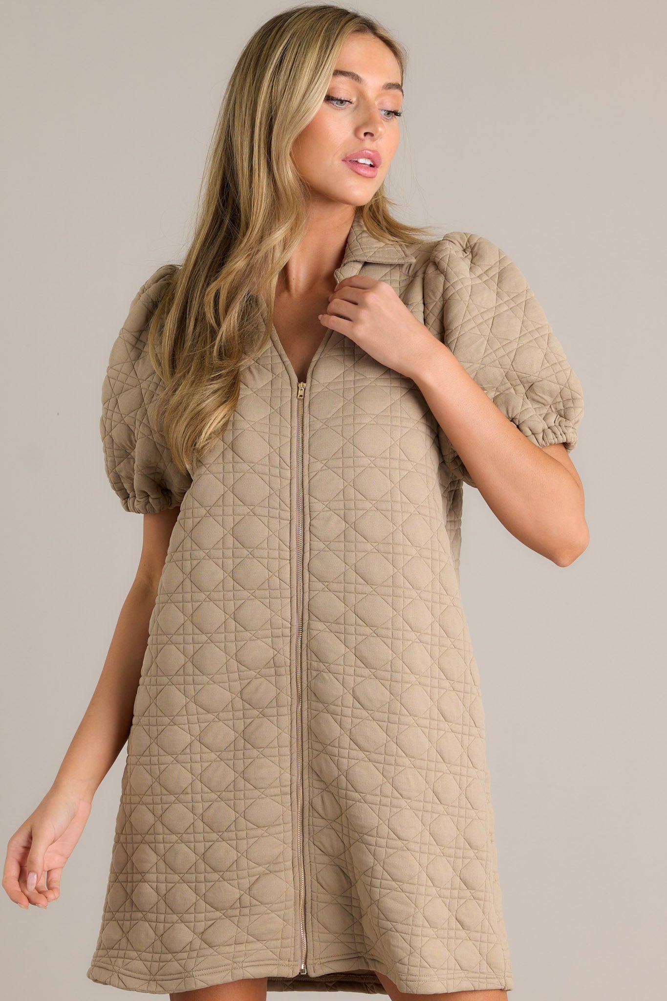 A tan quilted mini dress with a full-zip front, short puff sleeves, and a stylish collared neckline.