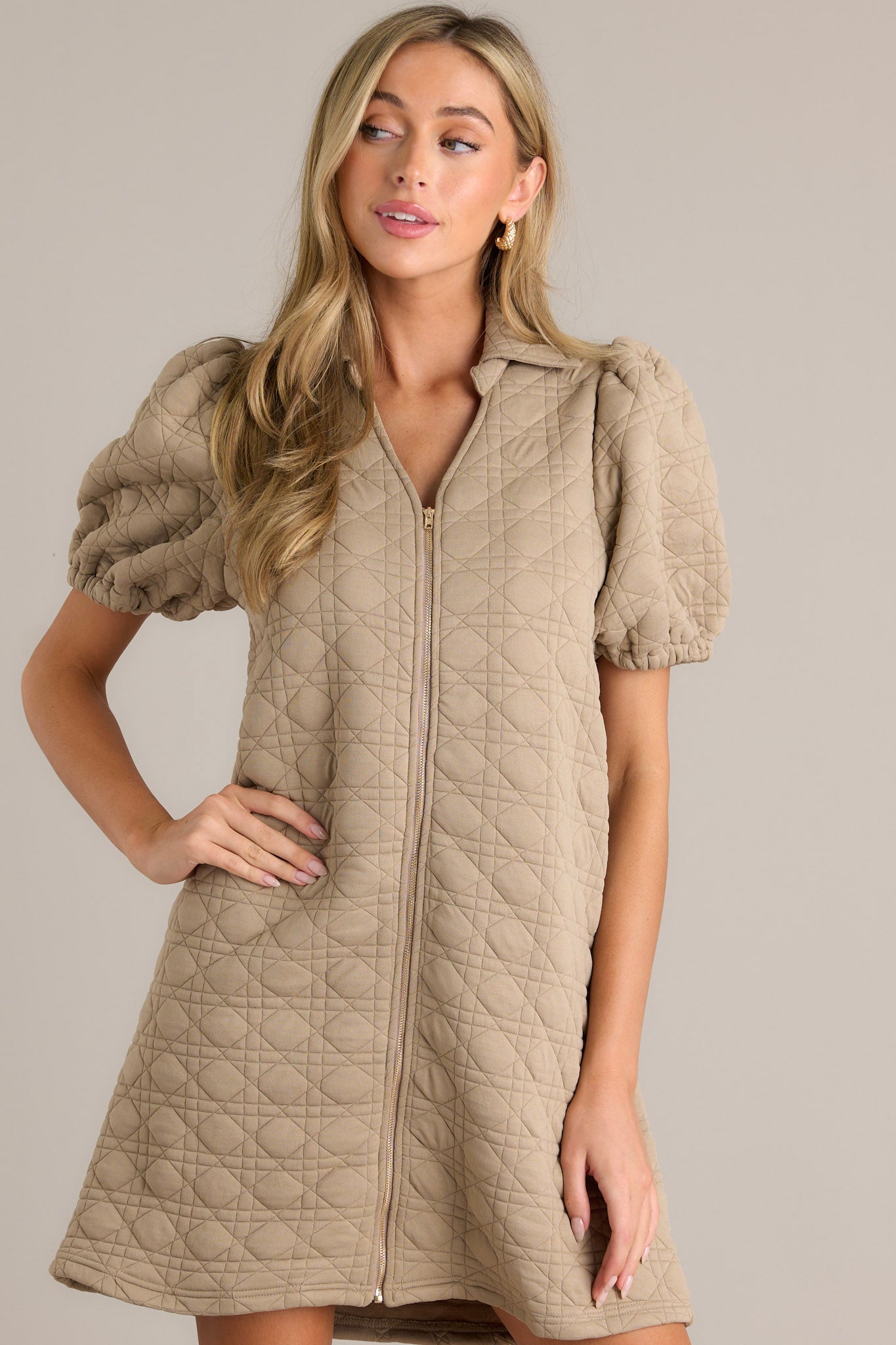 Front view of this tan quilted mini dress with a full zipper, short puff sleeves, and a trendy collared neckline.