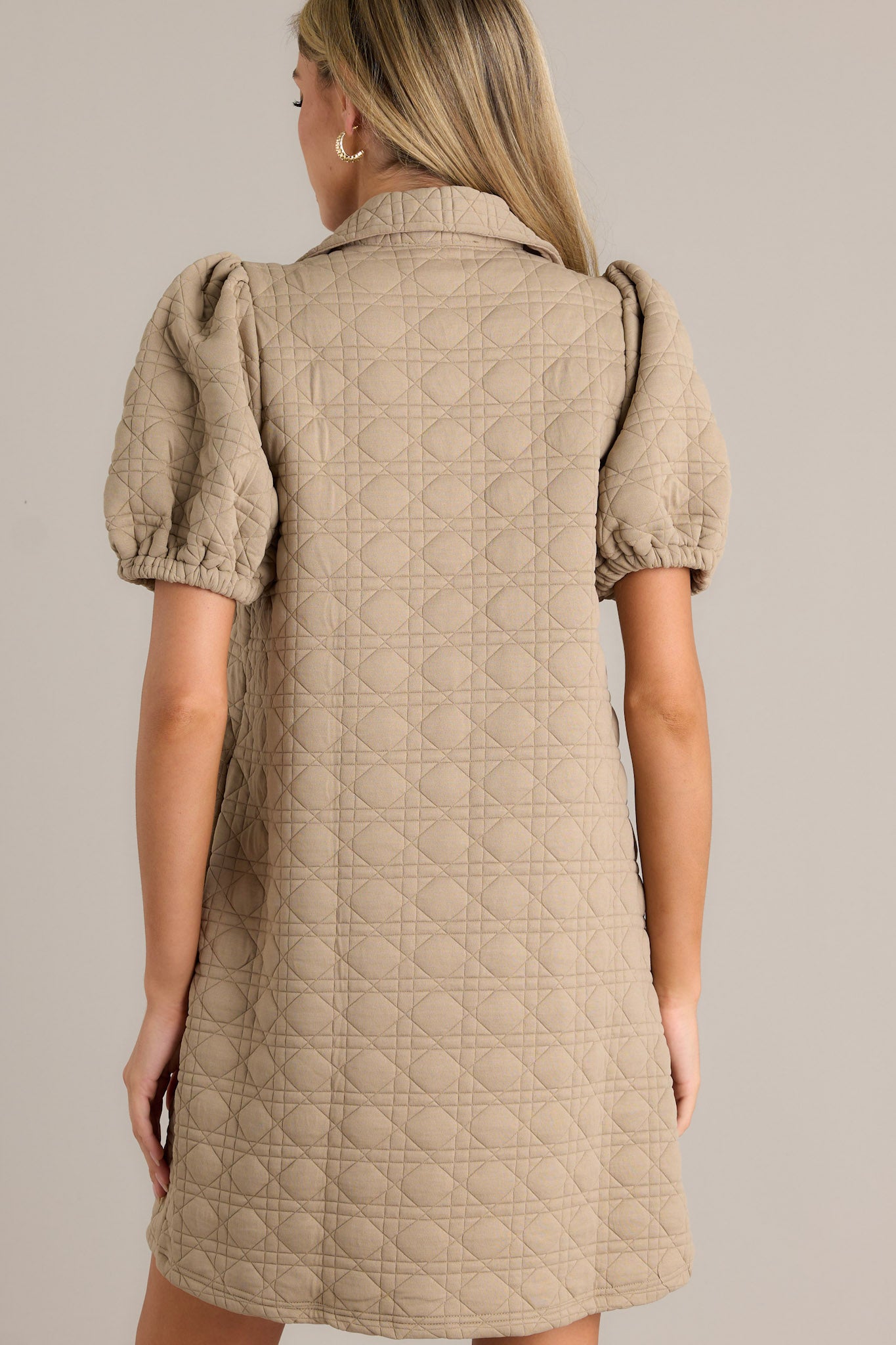 Back view of this tan quilted mini dress, complete with a full-zip front, and short puff sleeves.