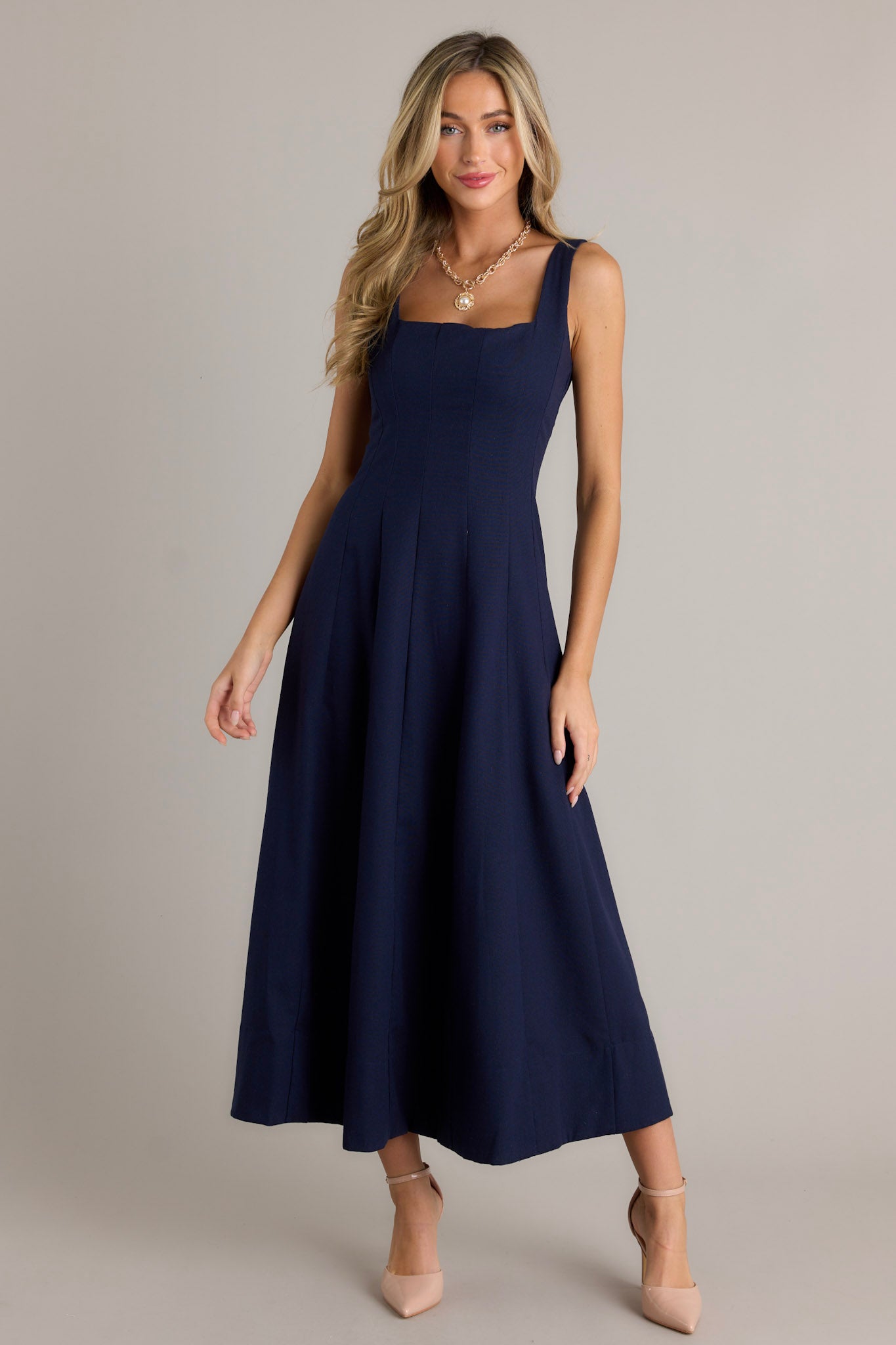 This navy maxi dress features a square neckline, thick straps, a discrete back zipper, a flowing silhouette, and a thick hemline