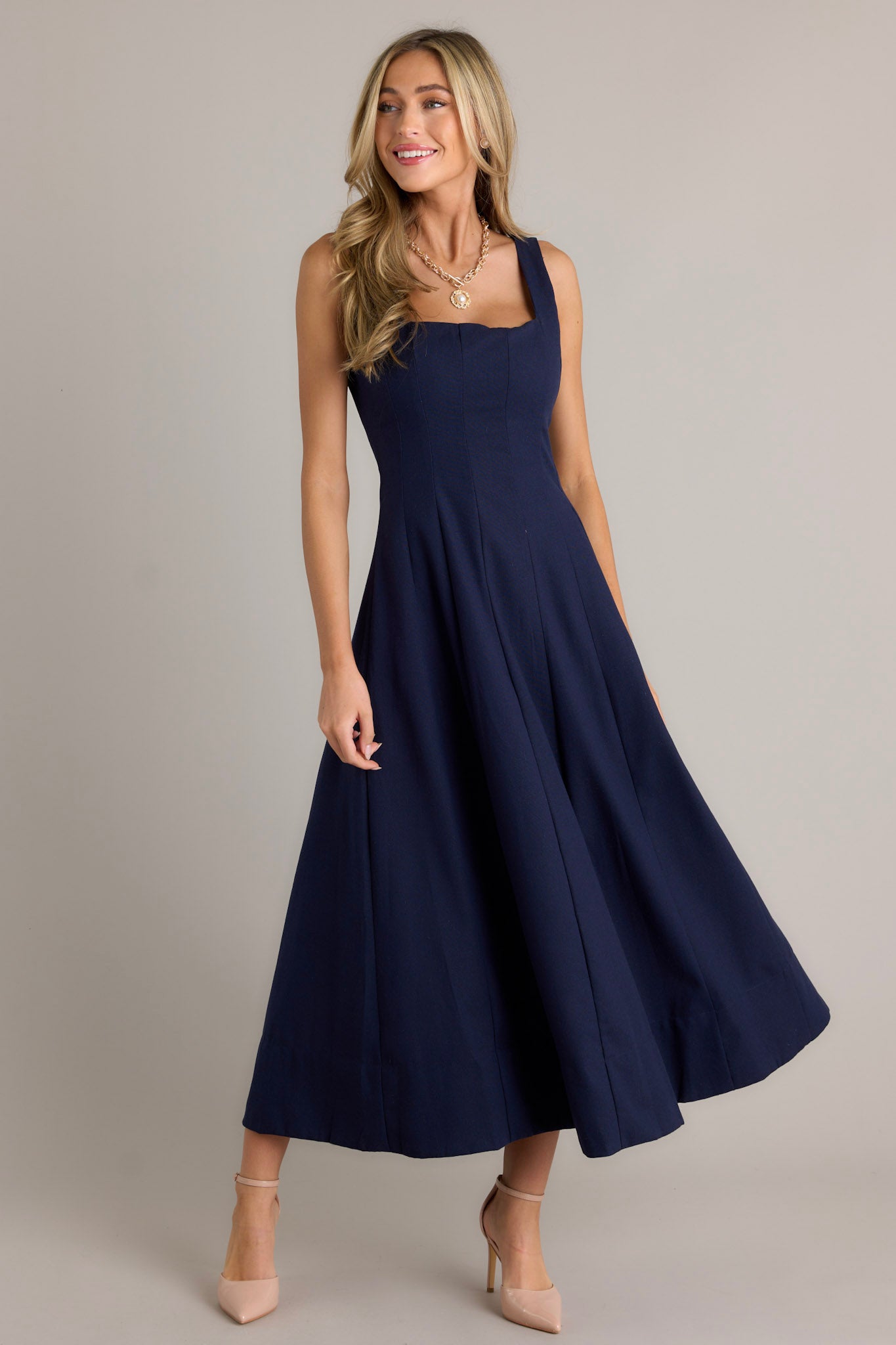 Action shot of a navy maxi dress displaying the fit and movement, highlighting the square neckline, thick straps, and the flowing silhouette.