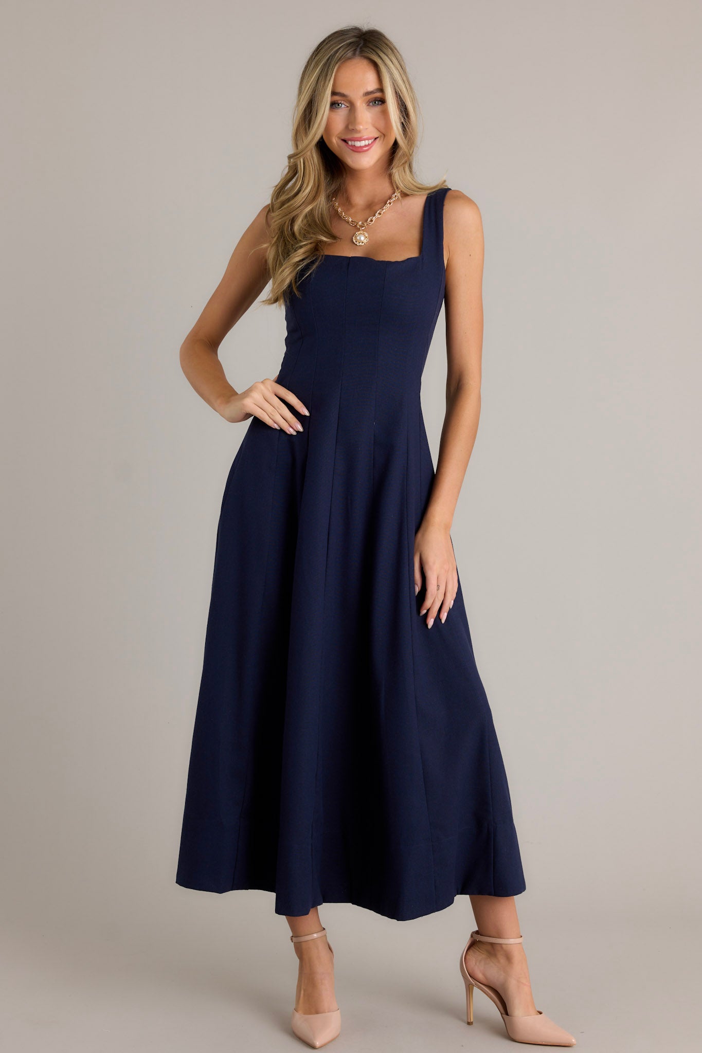 Front view of a navy maxi dress featuring a square neckline, thick straps, a discrete back zipper, a flowing silhouette, and a thick hemline.