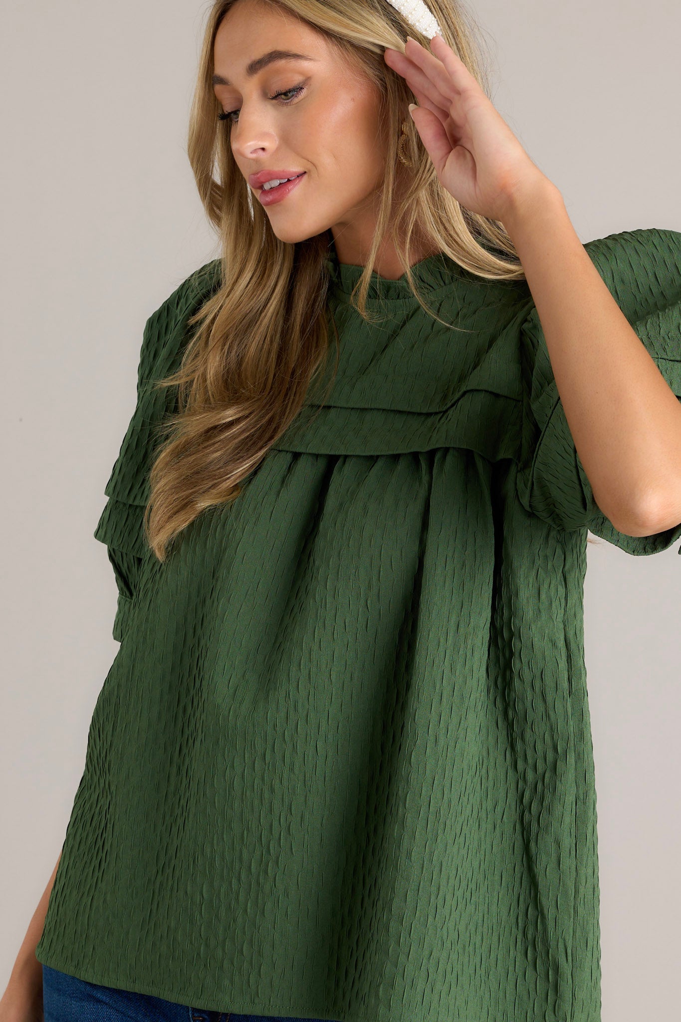 Side view of a green top showcasing the high ruffled neckline, short puff sleeves, and the textured seersucker fabric.