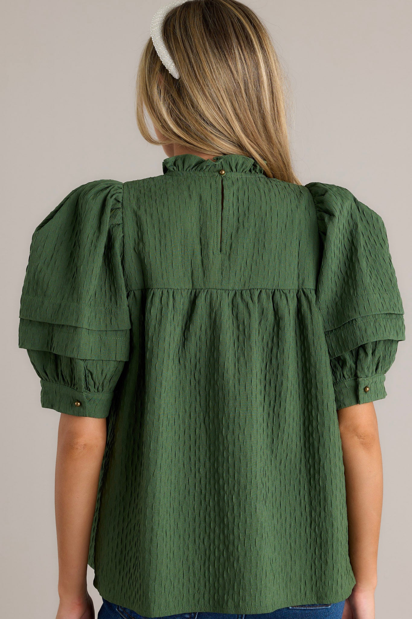 Back view of a green top highlighting the high ruffled neckline and the overall seersucker fabric.