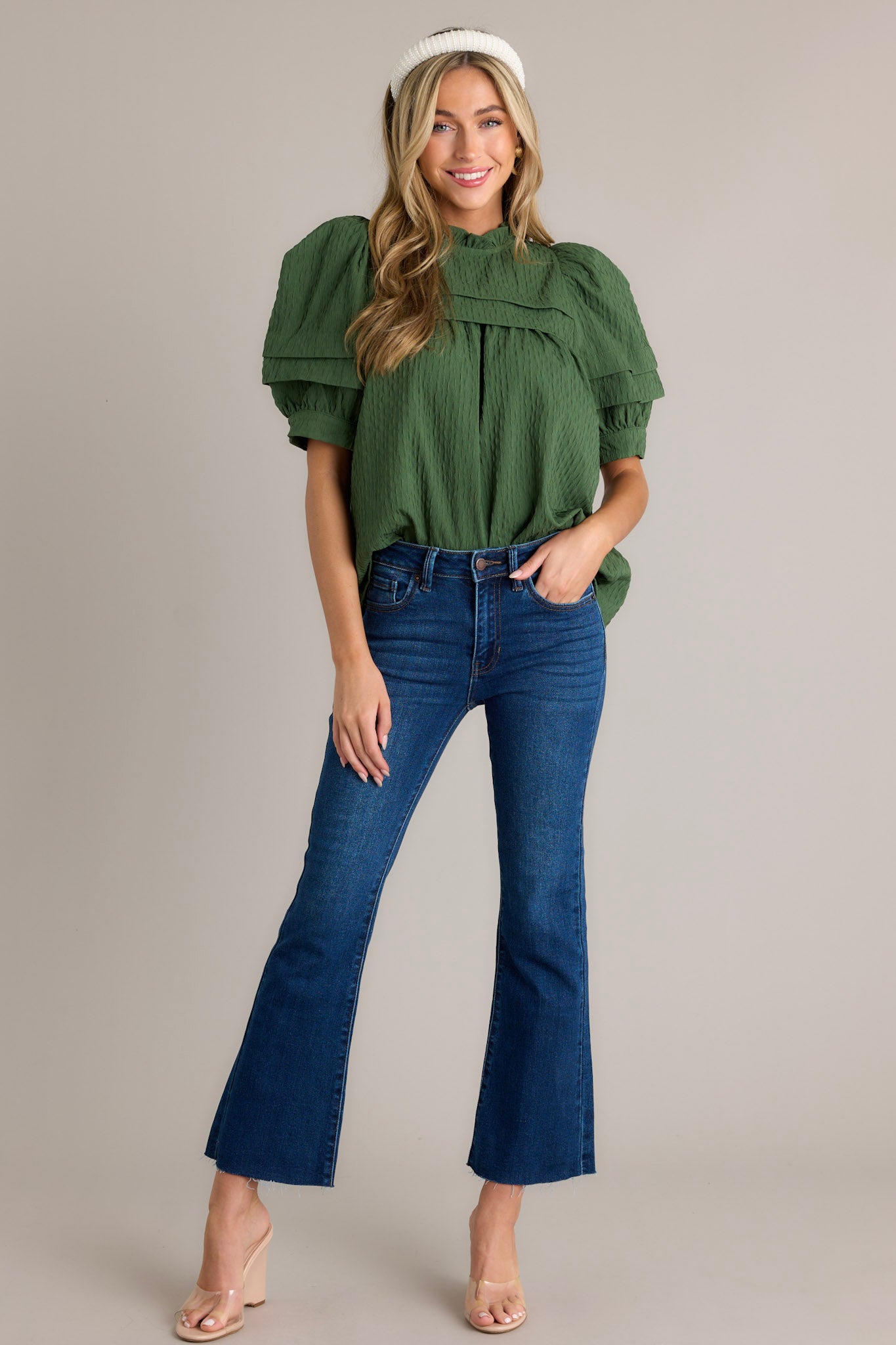 Front angled view of a green top featuring short puff sleeves, a high ruffled neckline, and a green seersucker fabric