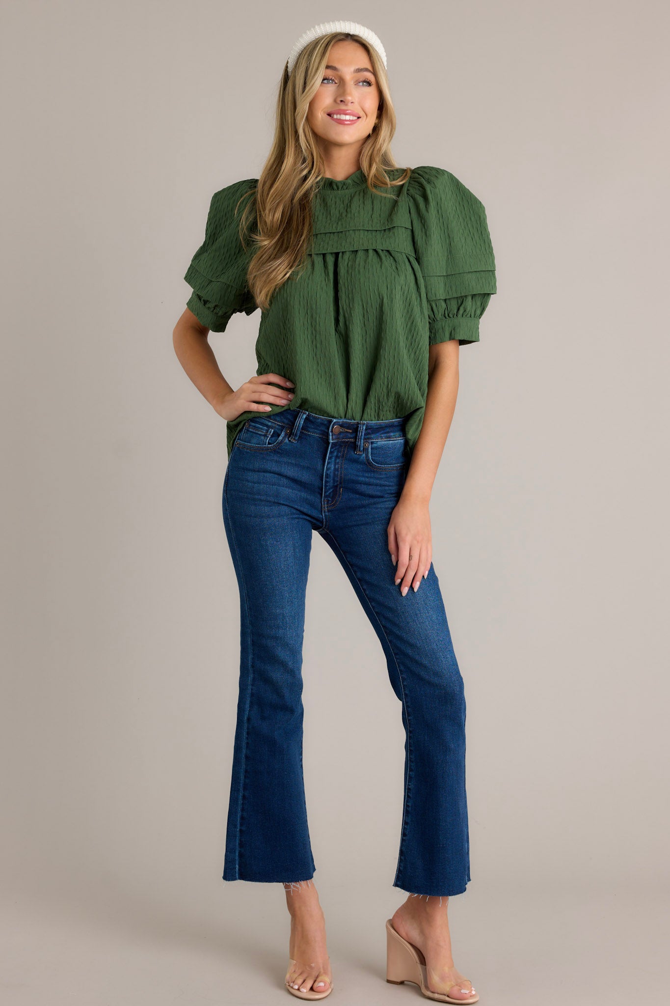 Full length view of a green top with short puff sleeves, a high ruffled neckline, and a green seersucker fabric