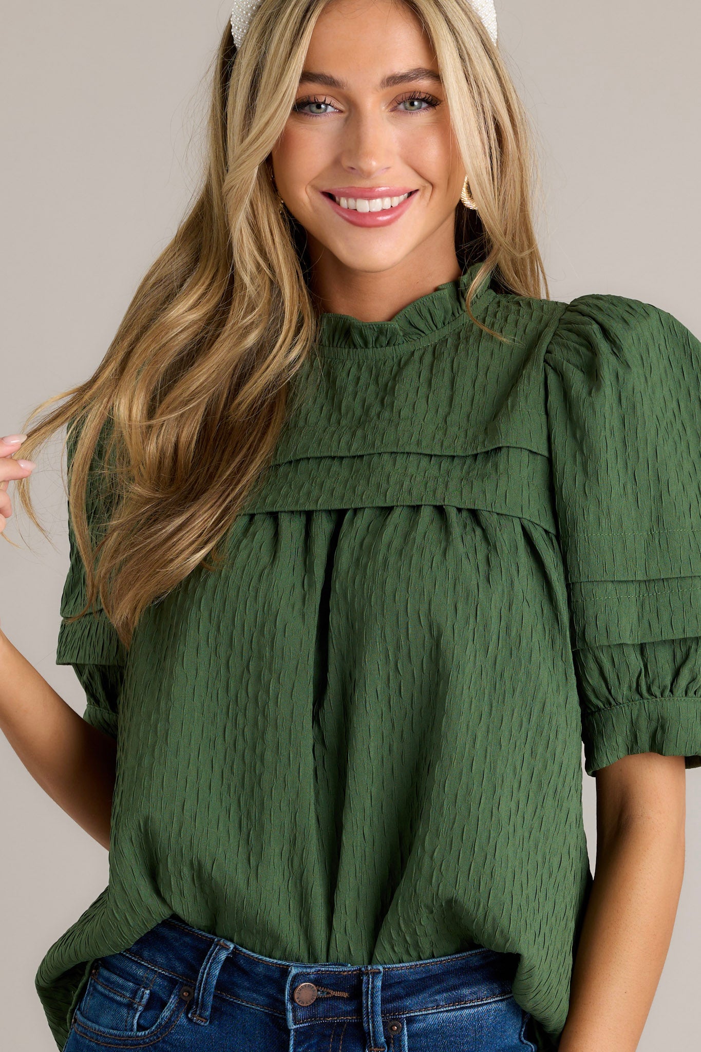 This green top features short puff sleeves, a high ruffled neckline, and a green seersucker fabric.