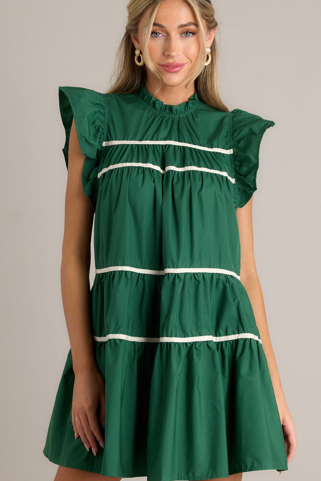 Front view of a green dress featuring ruffled sleeves, a round ruffle neckline, and two functional pockets.