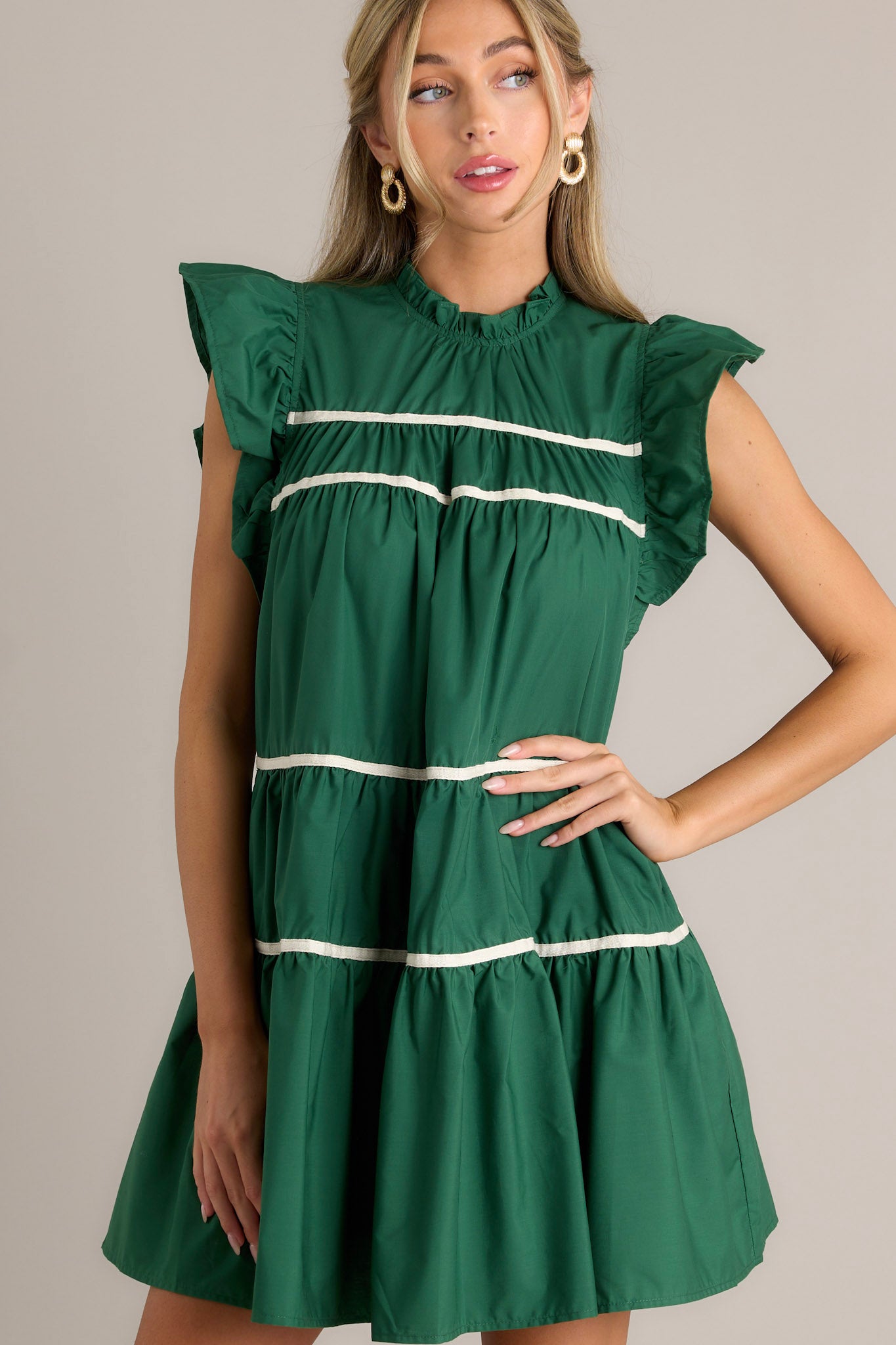 Front angled view of a green dress featuring ruffled sleeves, a round ruffle neckline, and two functional pockets